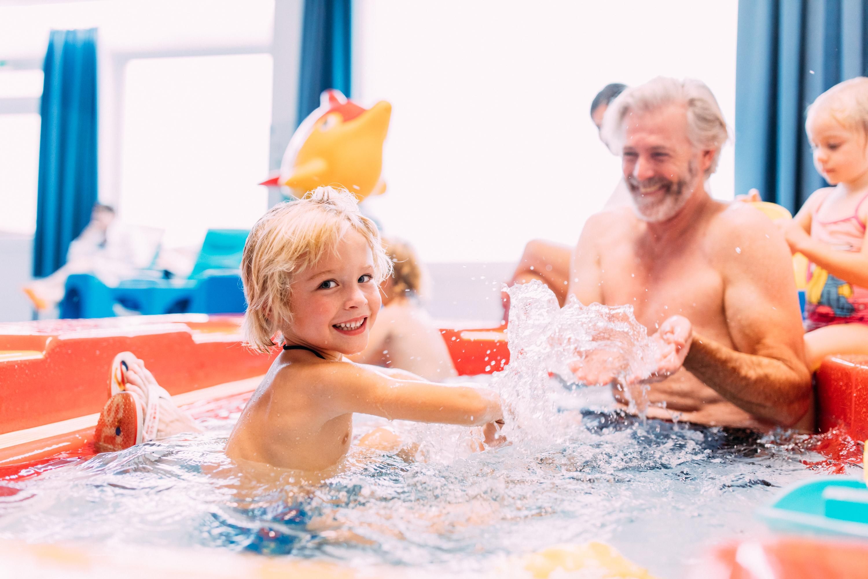 A happy child is playing in the water with an older man. They are enjoying their time together in the wading pool.