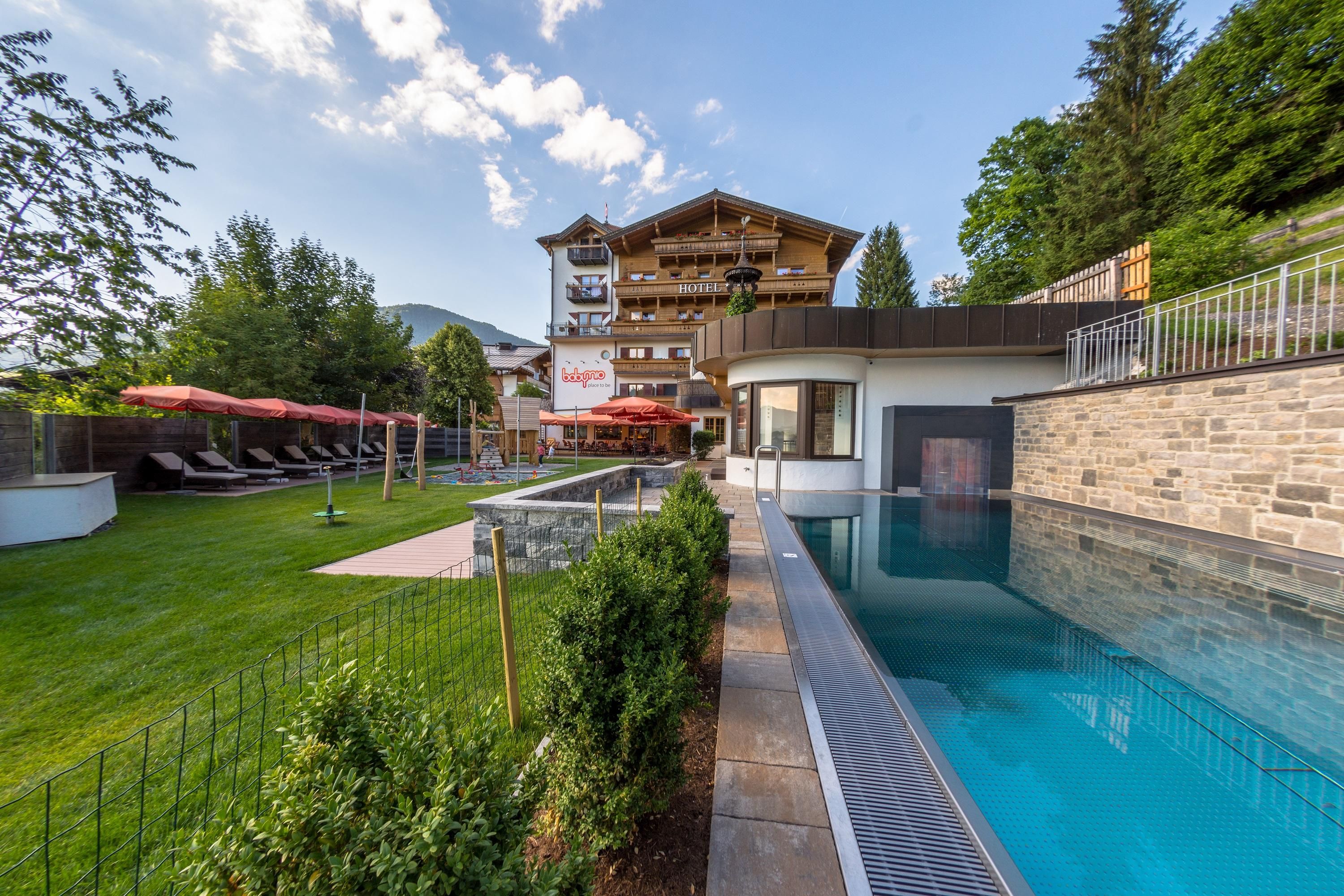 A beautiful outdoor area with a pool and loungers. In the background stands a charming building amidst trees.