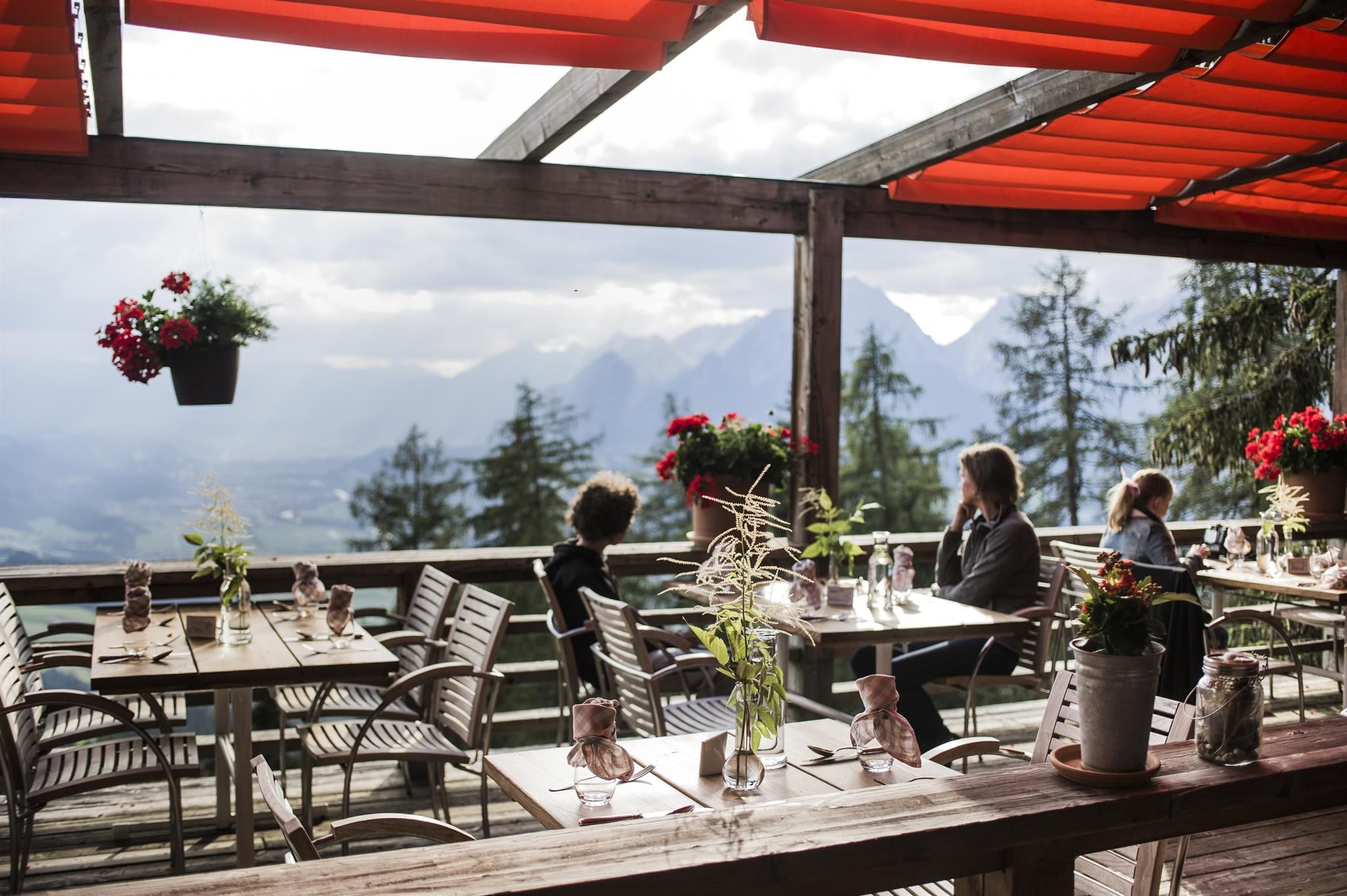 A cozy restaurant with a view of the mountains. The terrace is decorated with flowers and guests enjoy the scenery.