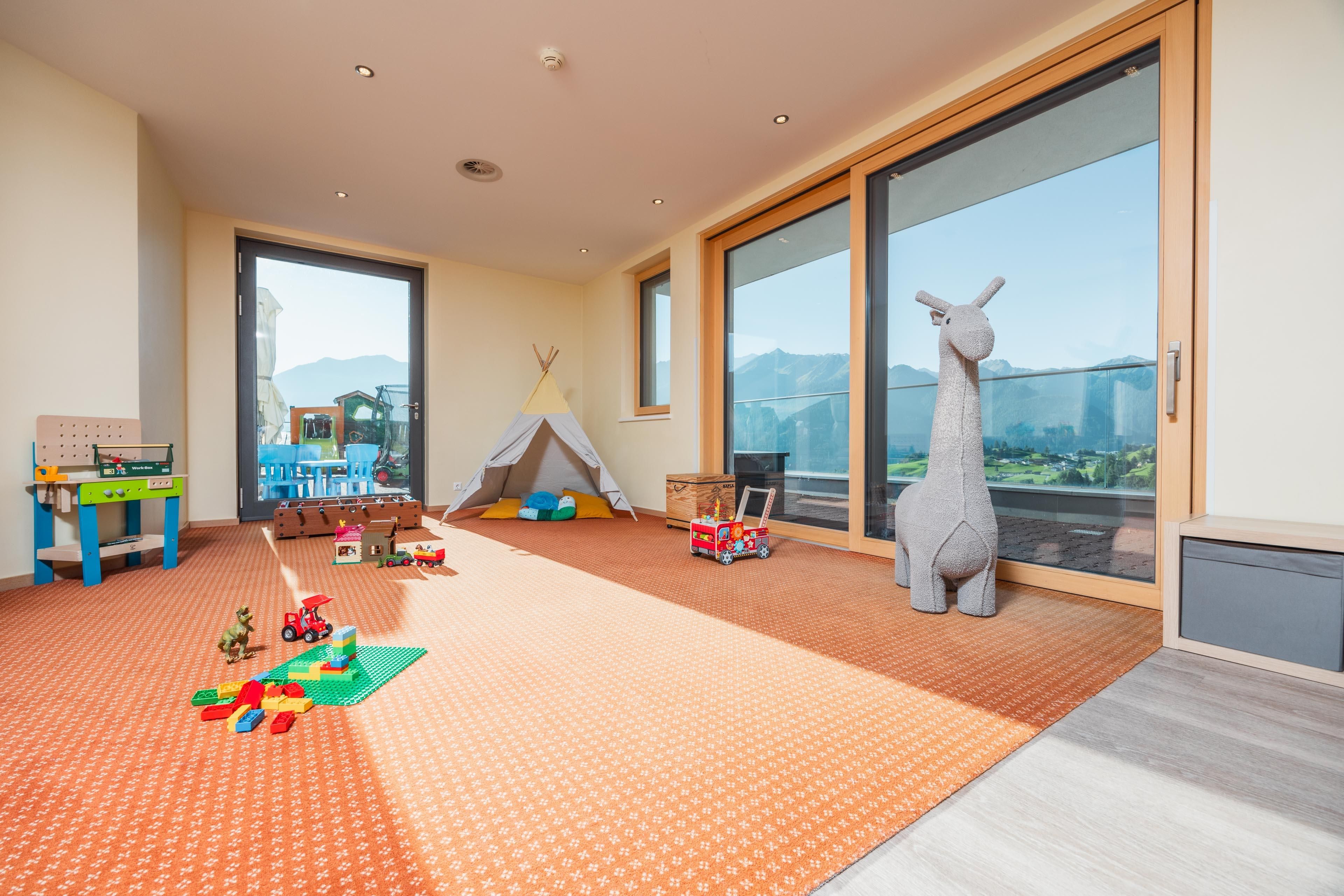 A bright playroom in the kids' club with a colorful carpet and large windows. Toys and a toy giraffe are visible, as well as a small tent for children.
