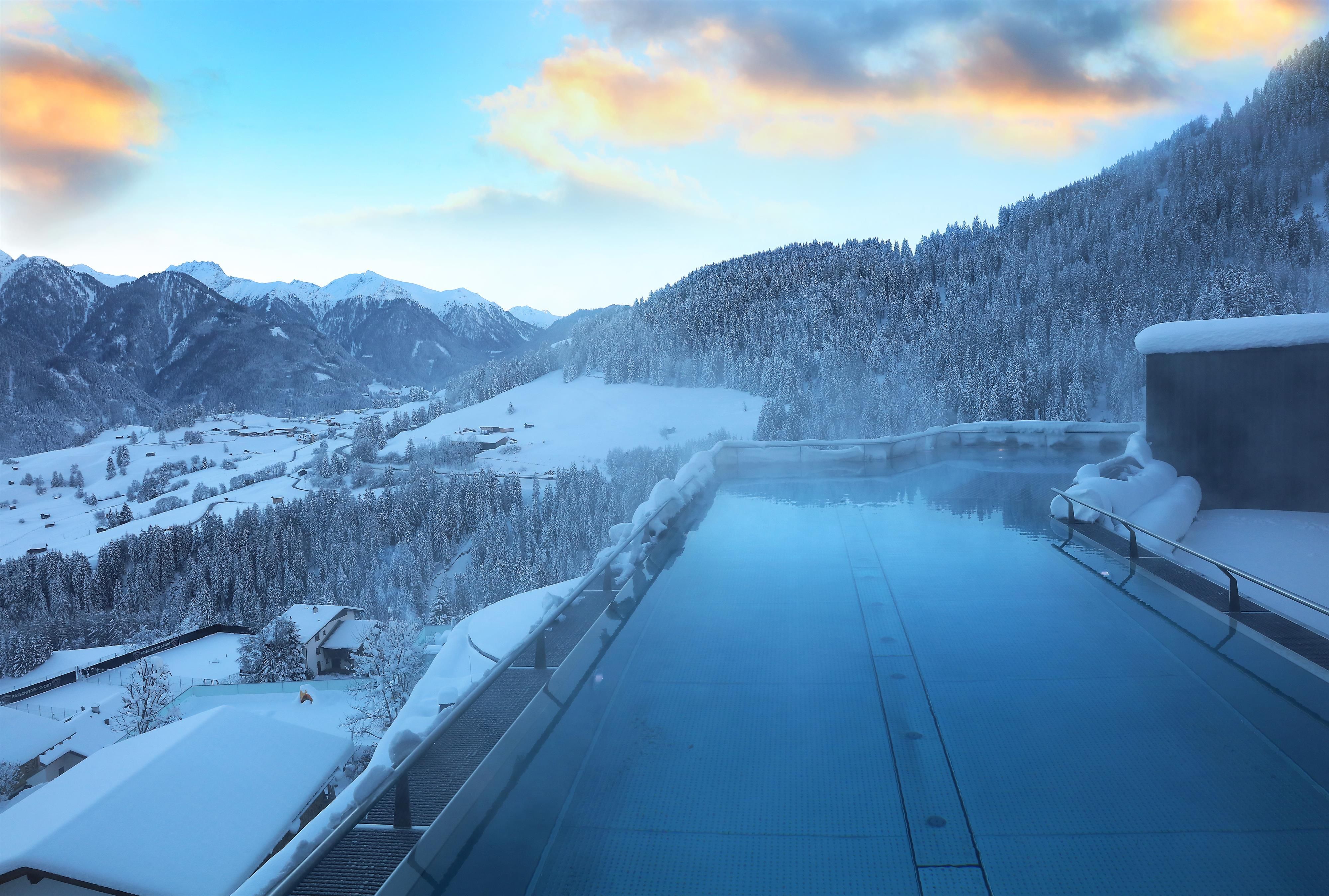 An infinity pool in the mountains, surrounded by snow-covered landscapes. The scene radiates peace and relaxation in a winter setting.