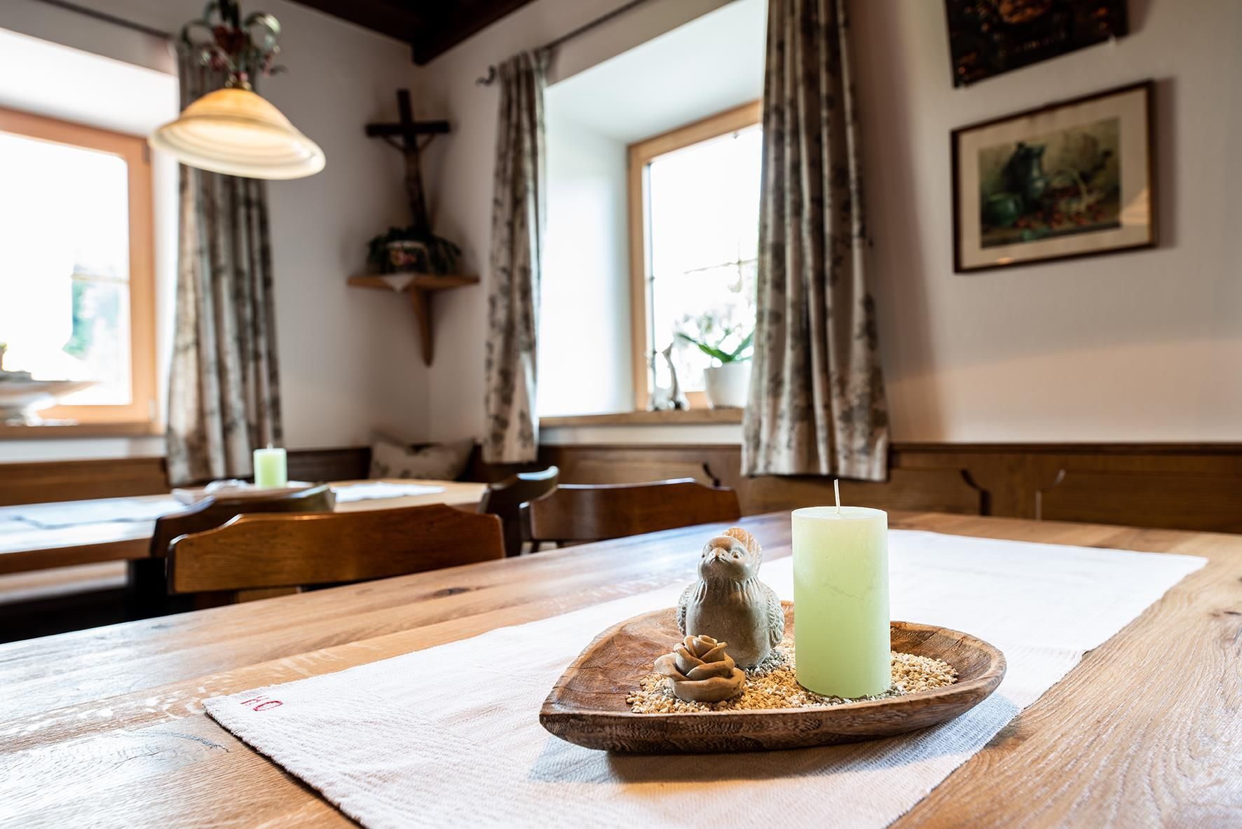 A cozy room with wooden tables and decorative windows. On the table, there is a wooden bowl with a candle and some small details.