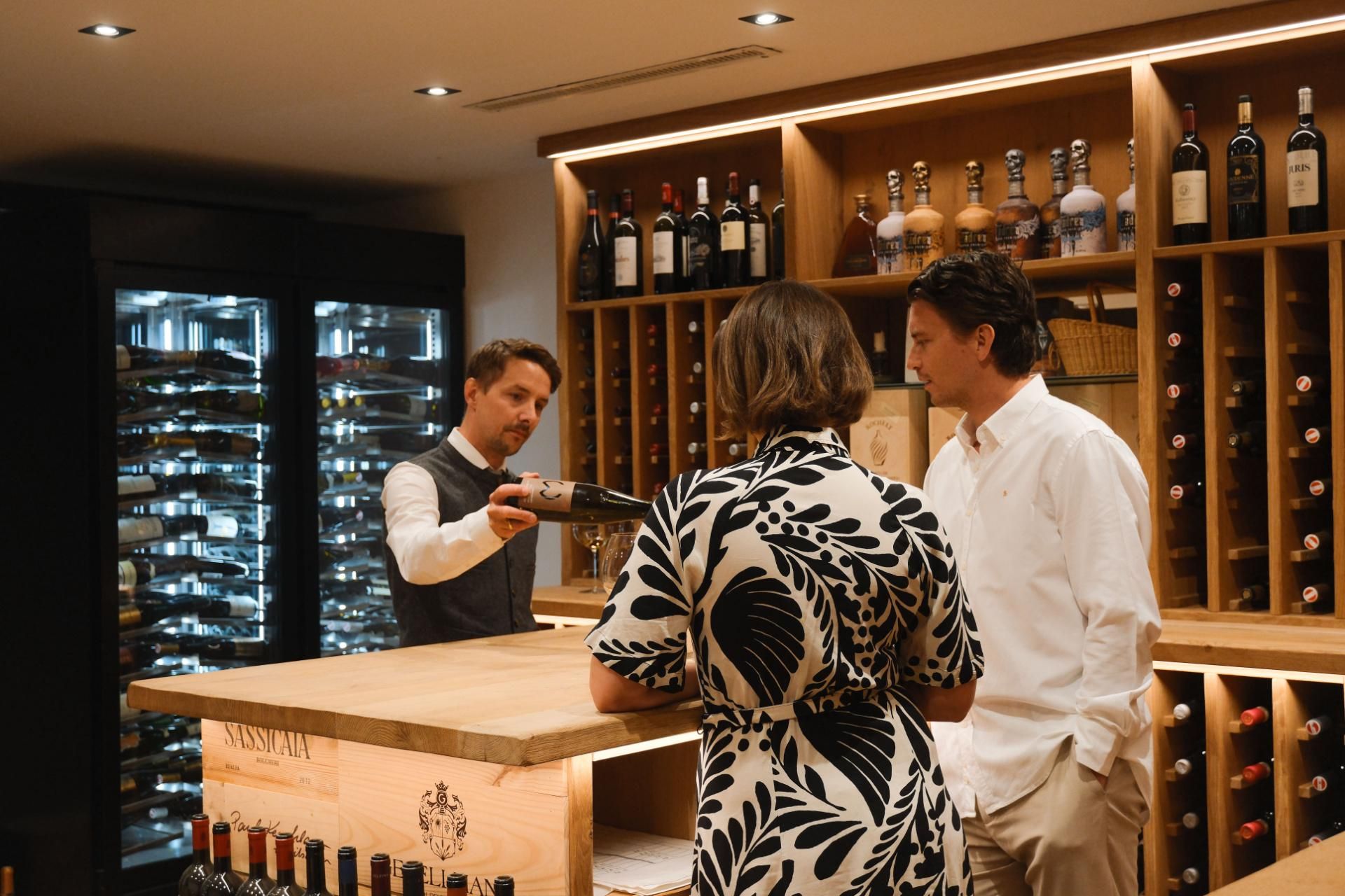 A wine tasting in a modern wine cellar. An employee presents wines to a woman and a man at a wooden counter.