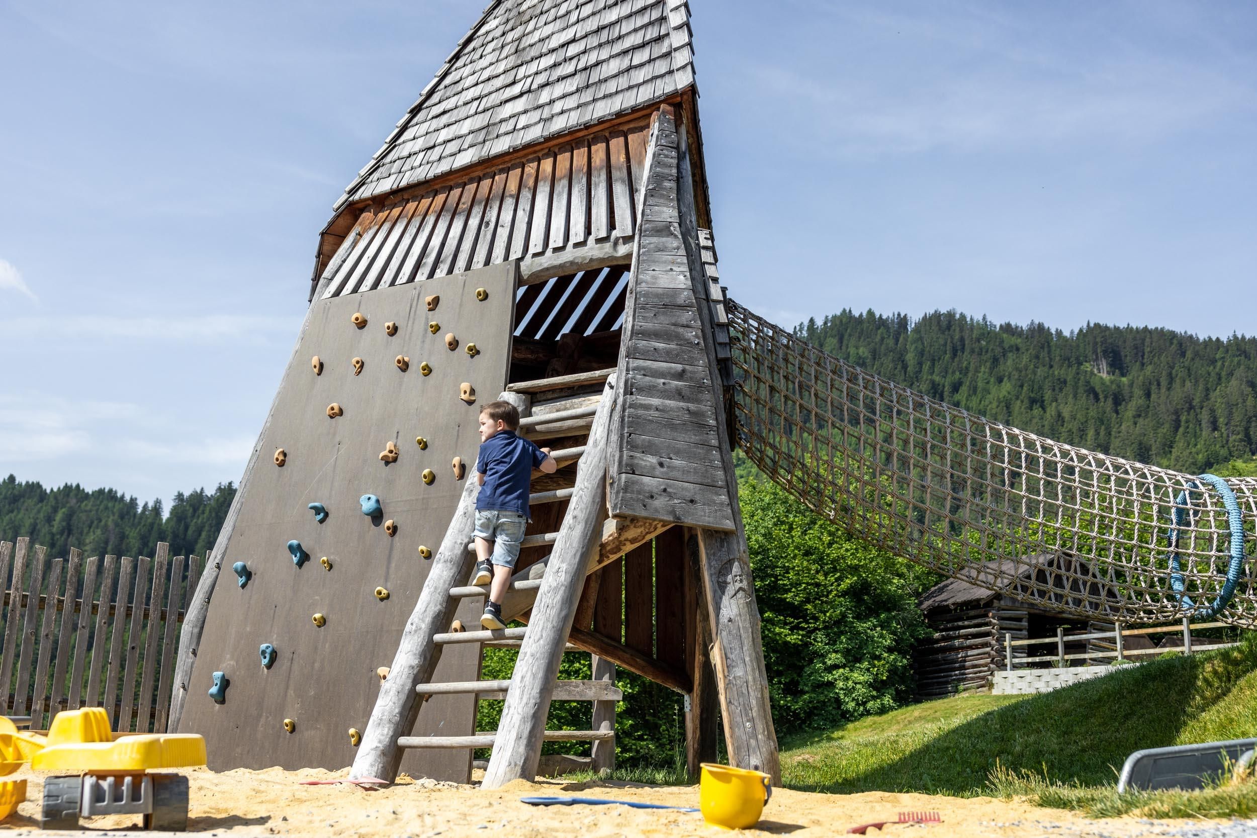 A beautiful playground with a wooden climbing frame. A child is playing and climbing on the wall.