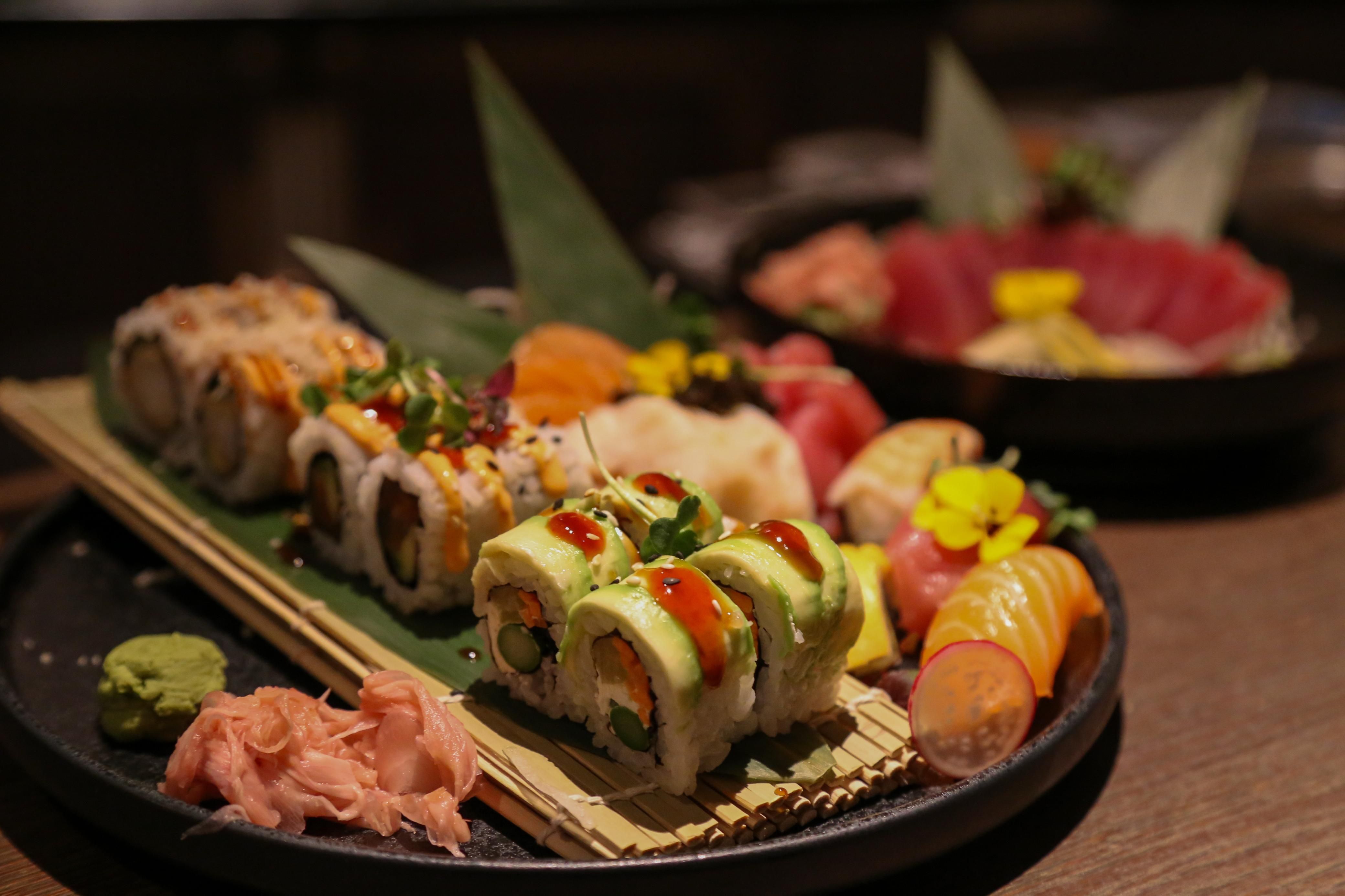 An appealing sushi arrangement with various rolls and fresh fish. Accompanied by decorative sides such as wasabi and ginger.