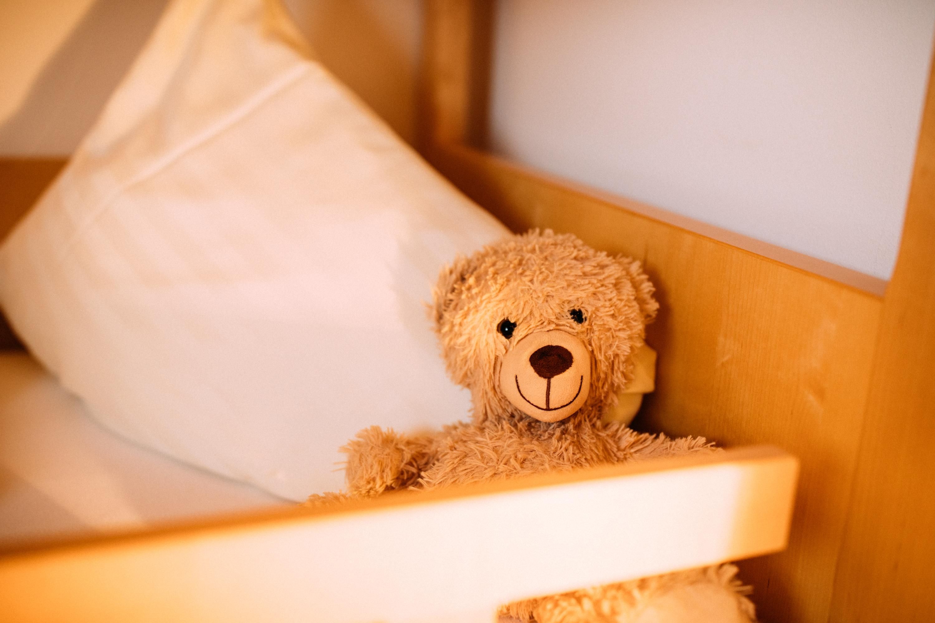 A soft teddy bear sits on a bed next to a pillow. The surroundings are warm and inviting.