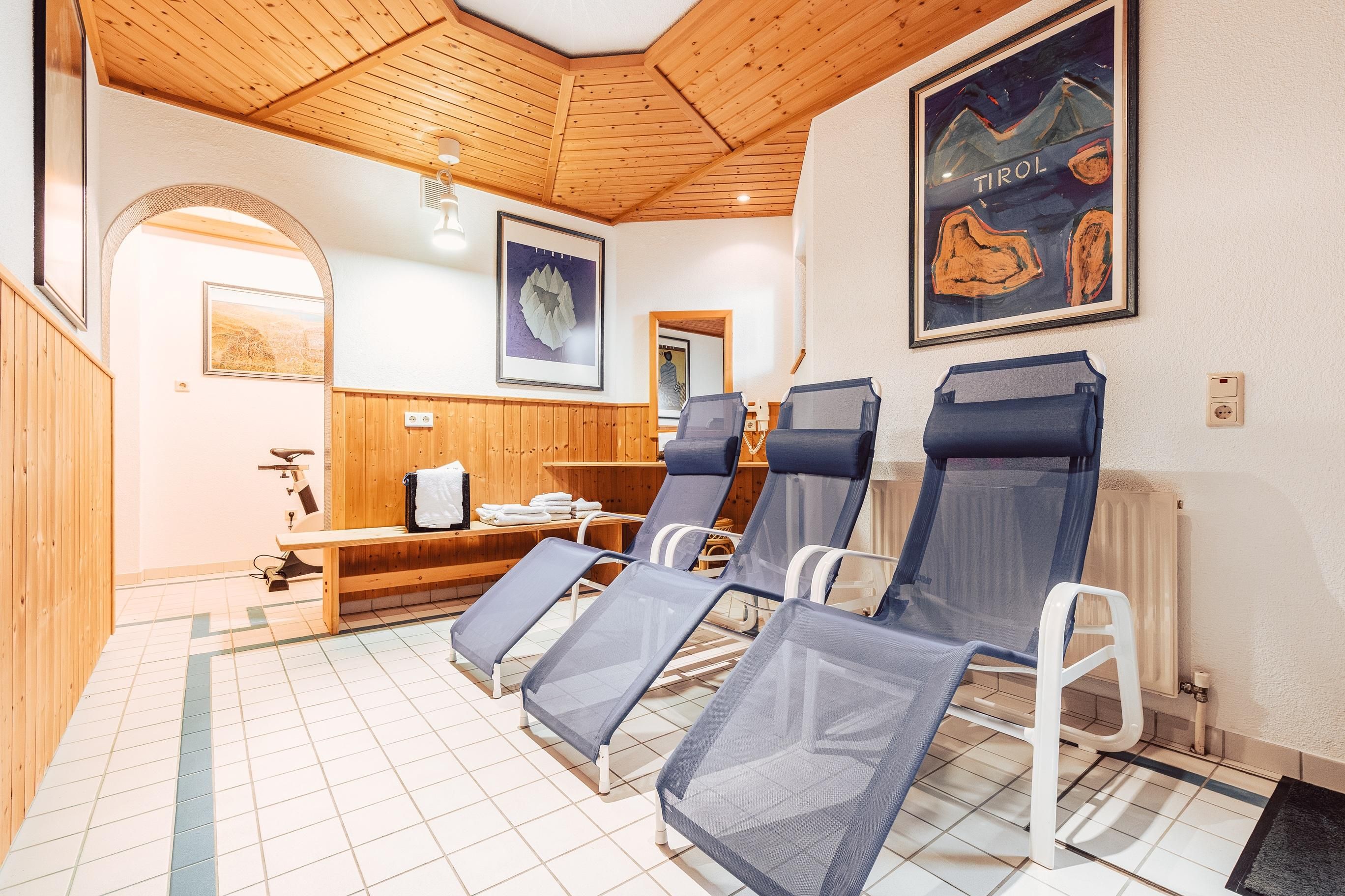 A relaxing room with loungers and wooden paneling. The walls are adorned with pictures and the floor is tiled.