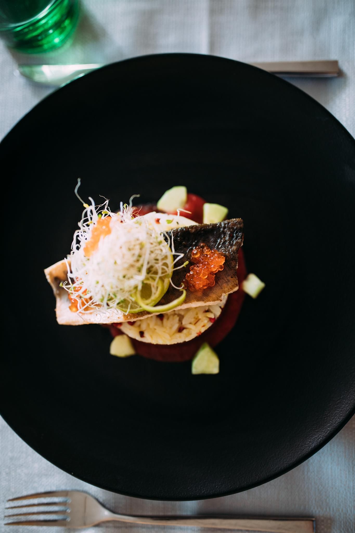 An artistically arranged plate with fish, fresh vegetables, and sprouts. The colors and textures make the dish especially appealing.