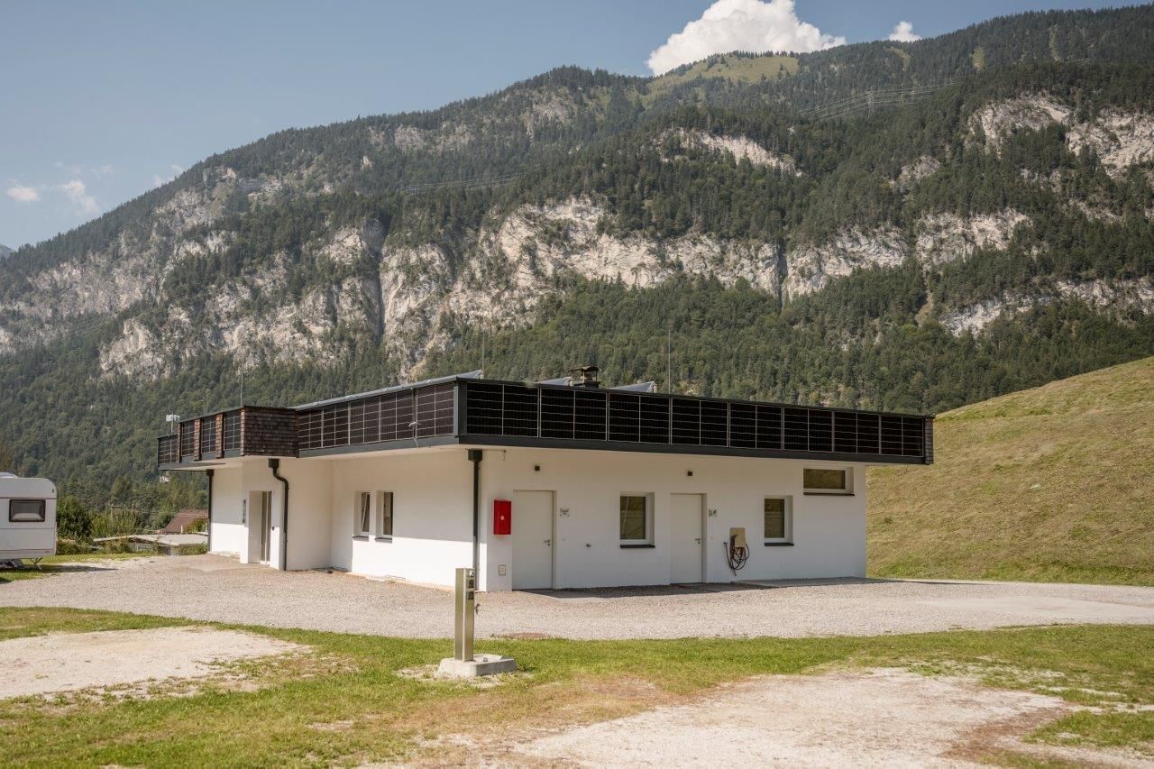 A modern house in a rural setting with mountains in the background. The façade is white and features a flat roof with large windows.