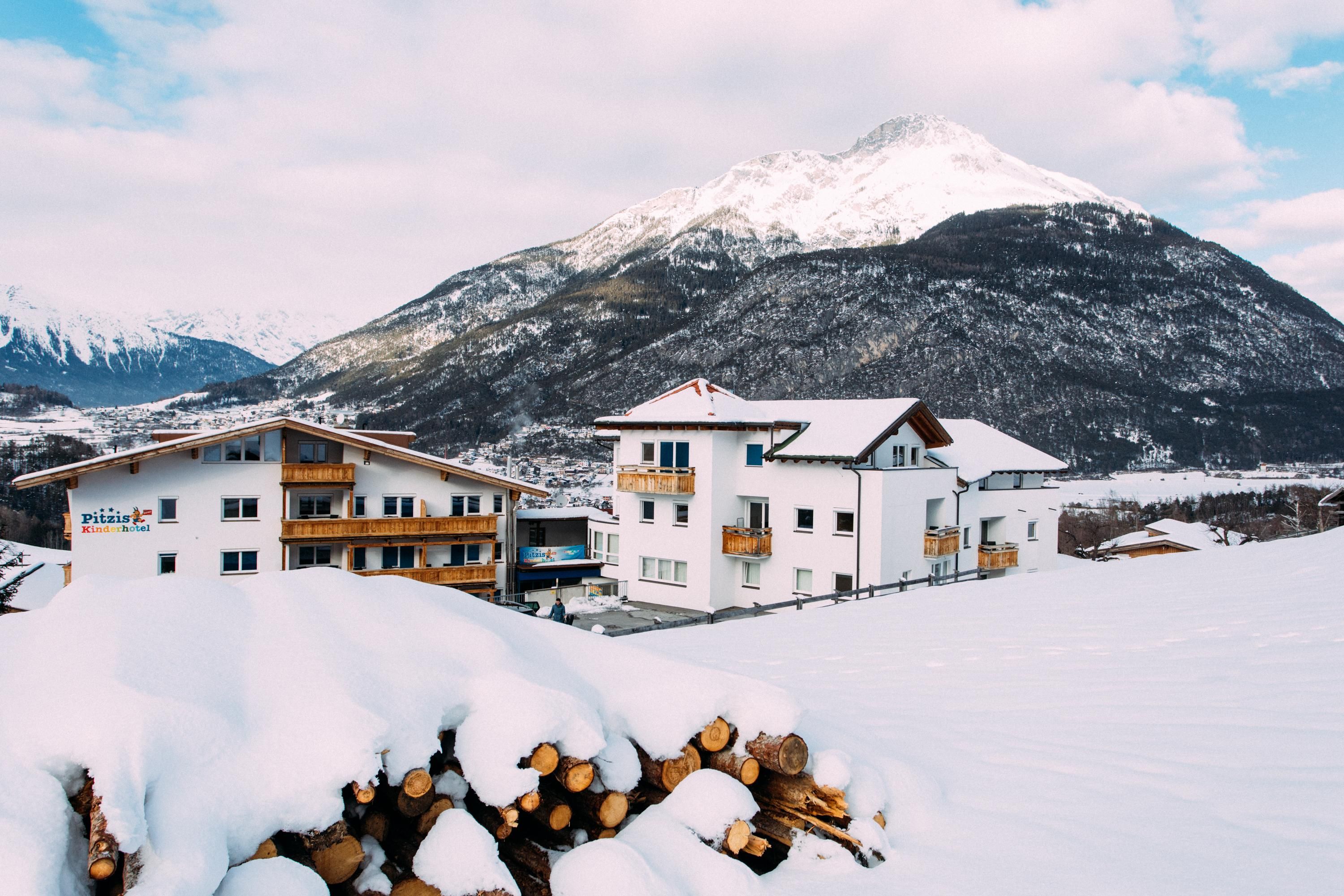Snow-covered mountains with a tranquil village in the foreground. Stacks of wood and charming buildings characterize the winter landscape.