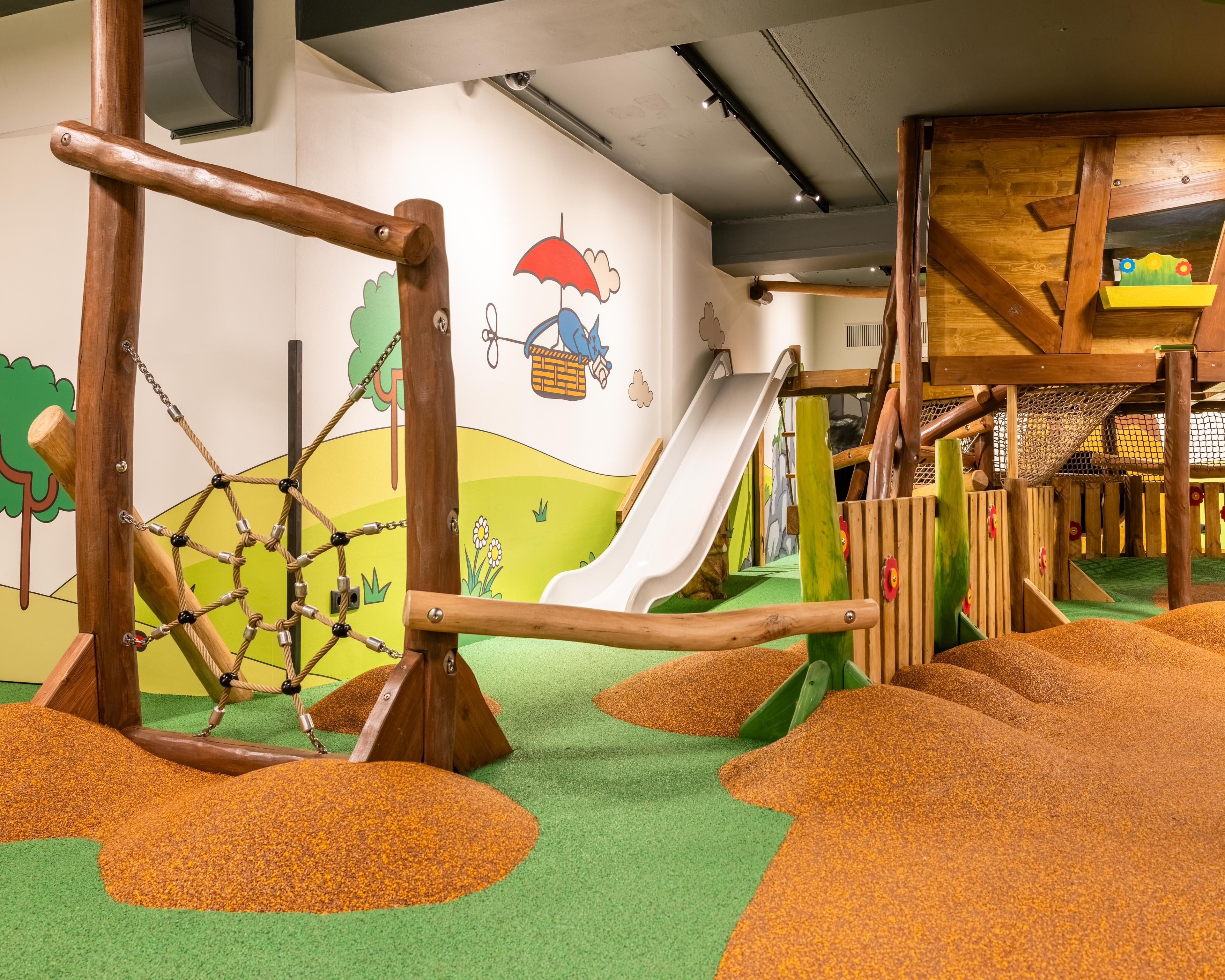 STAR.Landia - Indoor play area with a treehouse featuring a slide and climbing elements made of wood. The colorful environment is child-friendly and designed with a soft flooring.