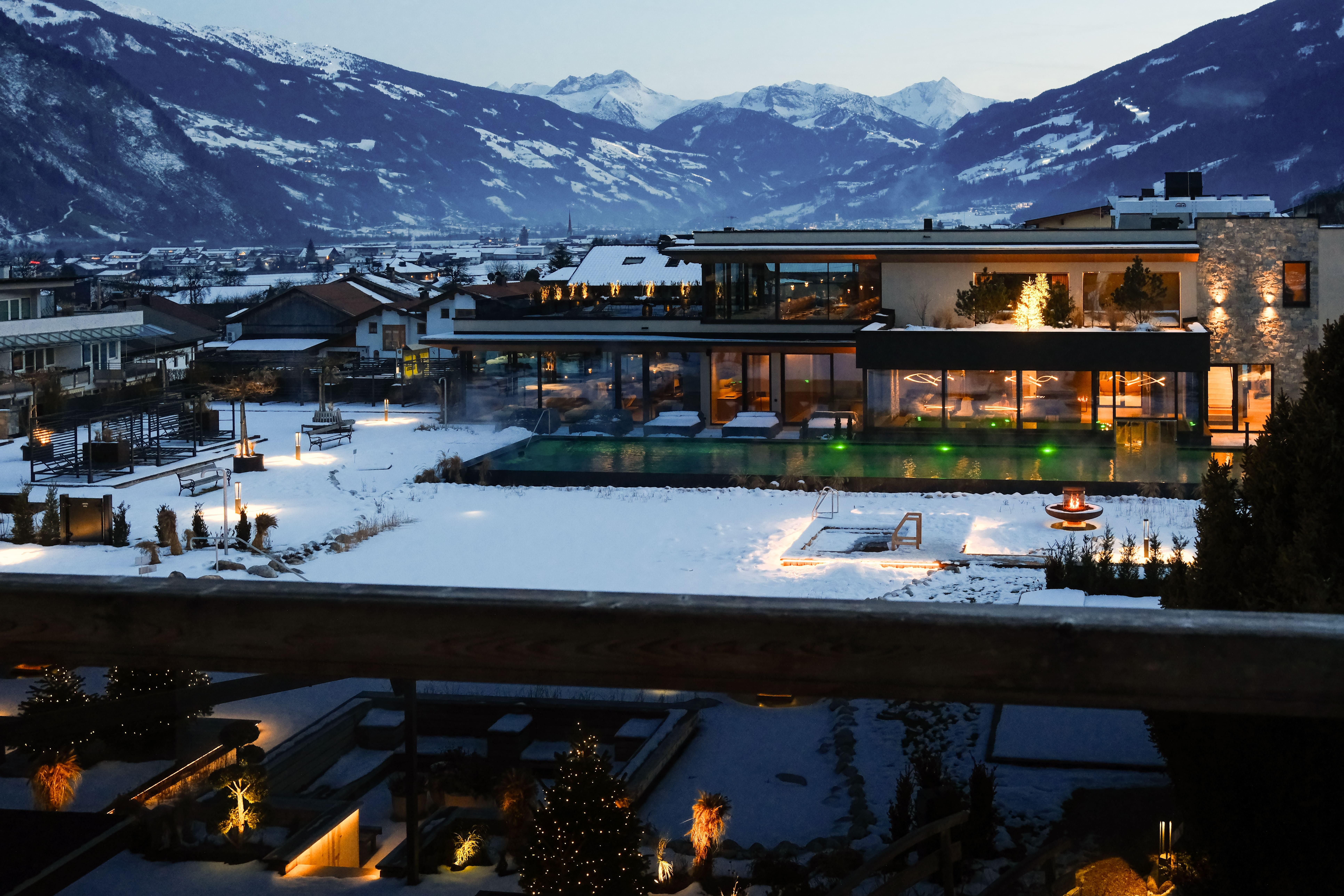 A modern building in a snowy landscape, surrounded by mountains. The interior and exterior lighting creates a cozy atmosphere at dusk.