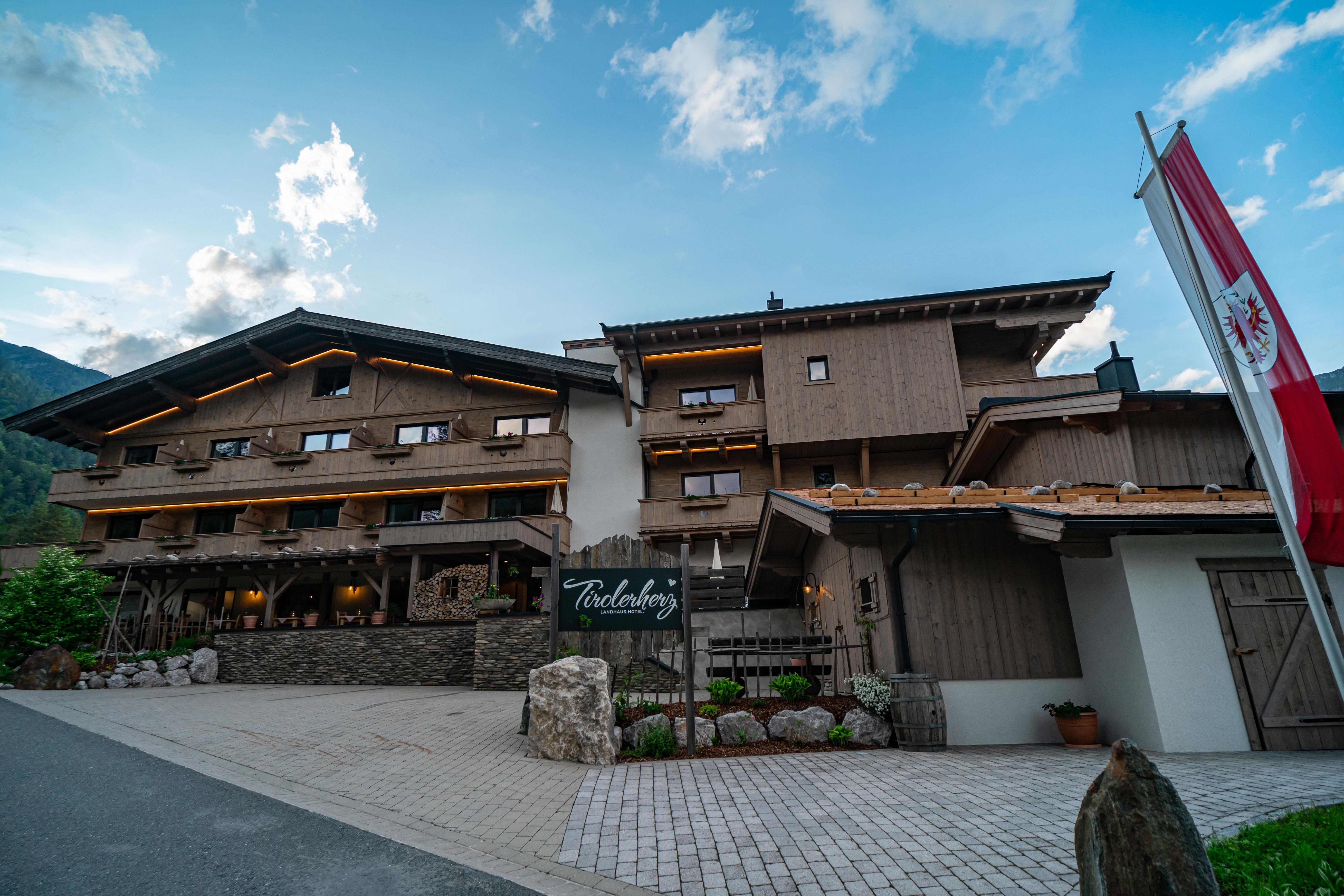 A modern hotel building in alpine style with wood cladding. The entrance area is invitingly designed and surrounded by a picturesque landscape.