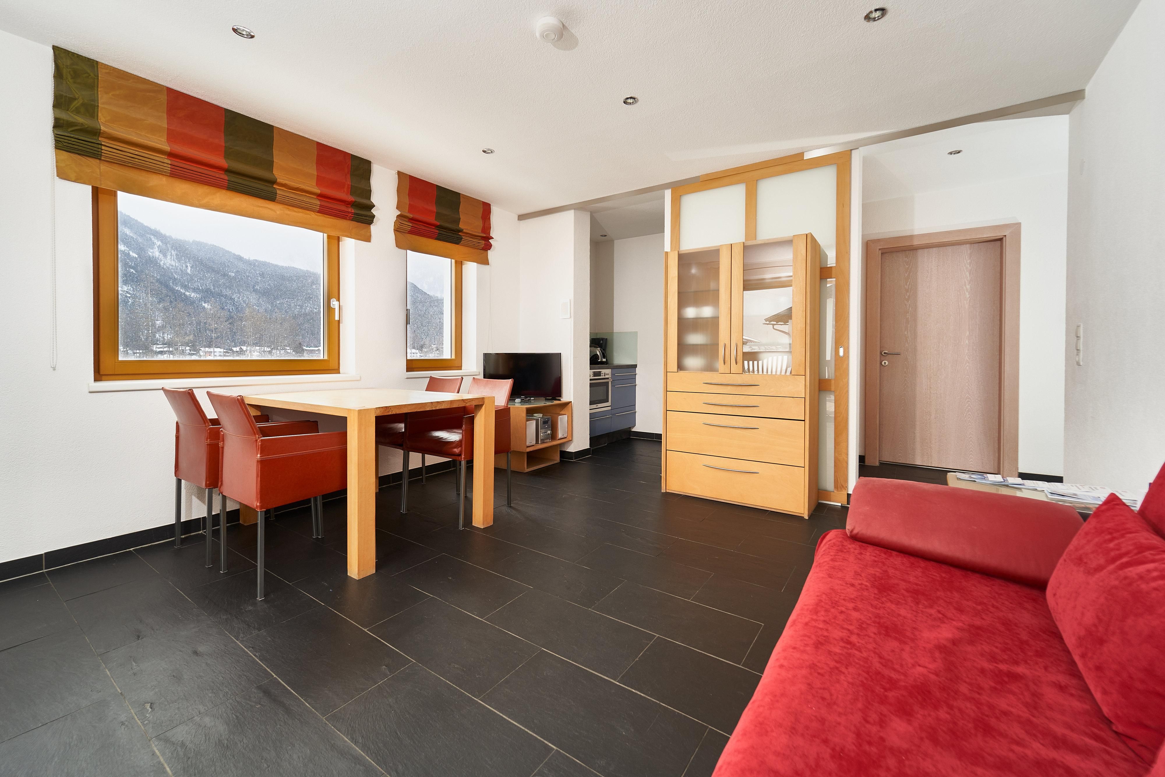 A modern apartment with a dining area that includes a table and chairs. The large windows offer a beautiful view of the mountains.