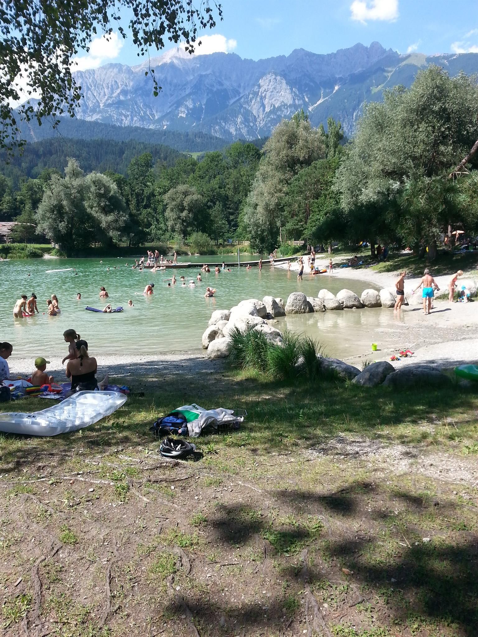 A beautiful swimming lake surrounded by trees and mountains. Many people enjoy the water on a sunny day.