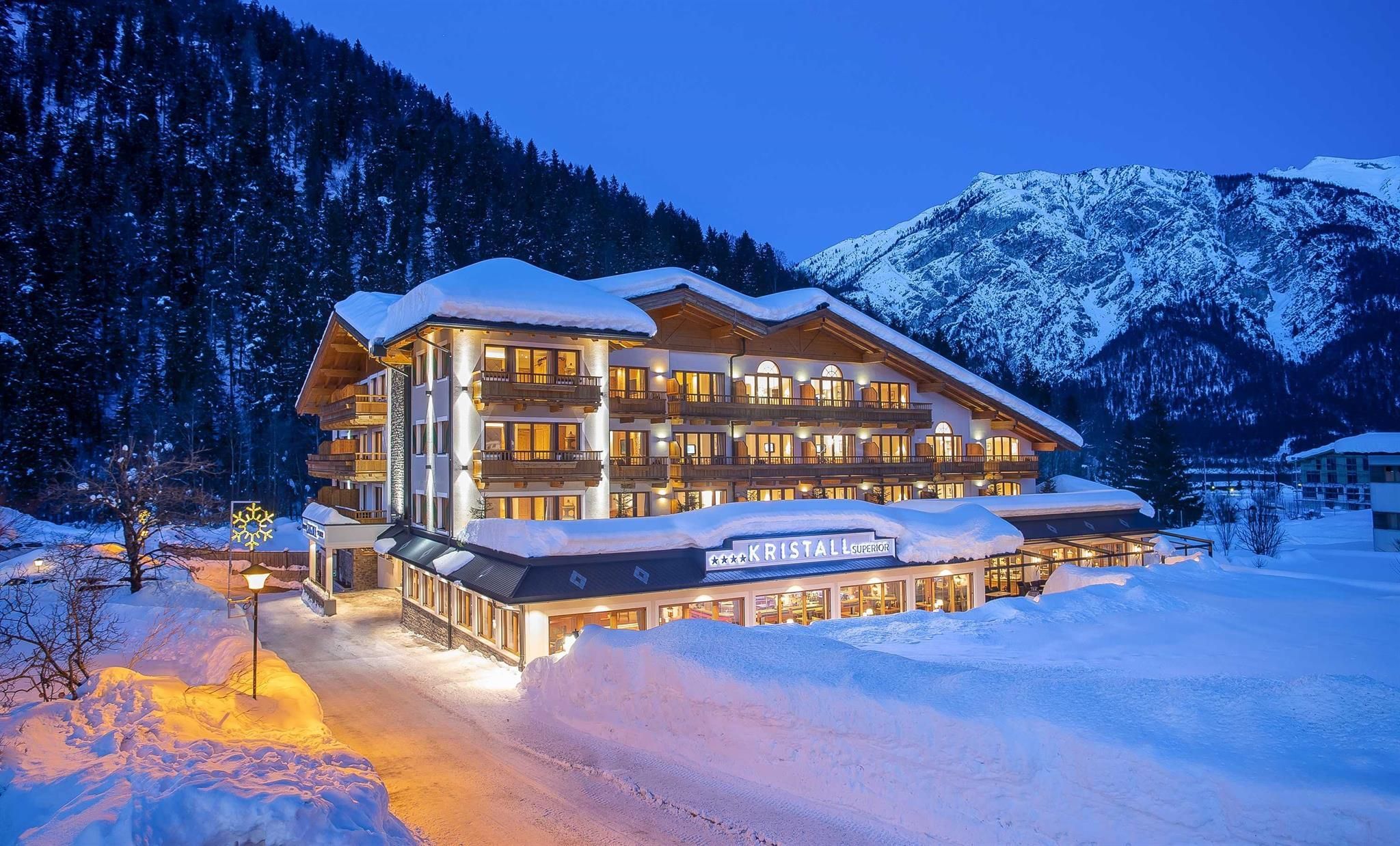 A charming hotel in the snow, surrounded by mountains. The facade is beautifully lit in the evening, creating a cozy atmosphere.