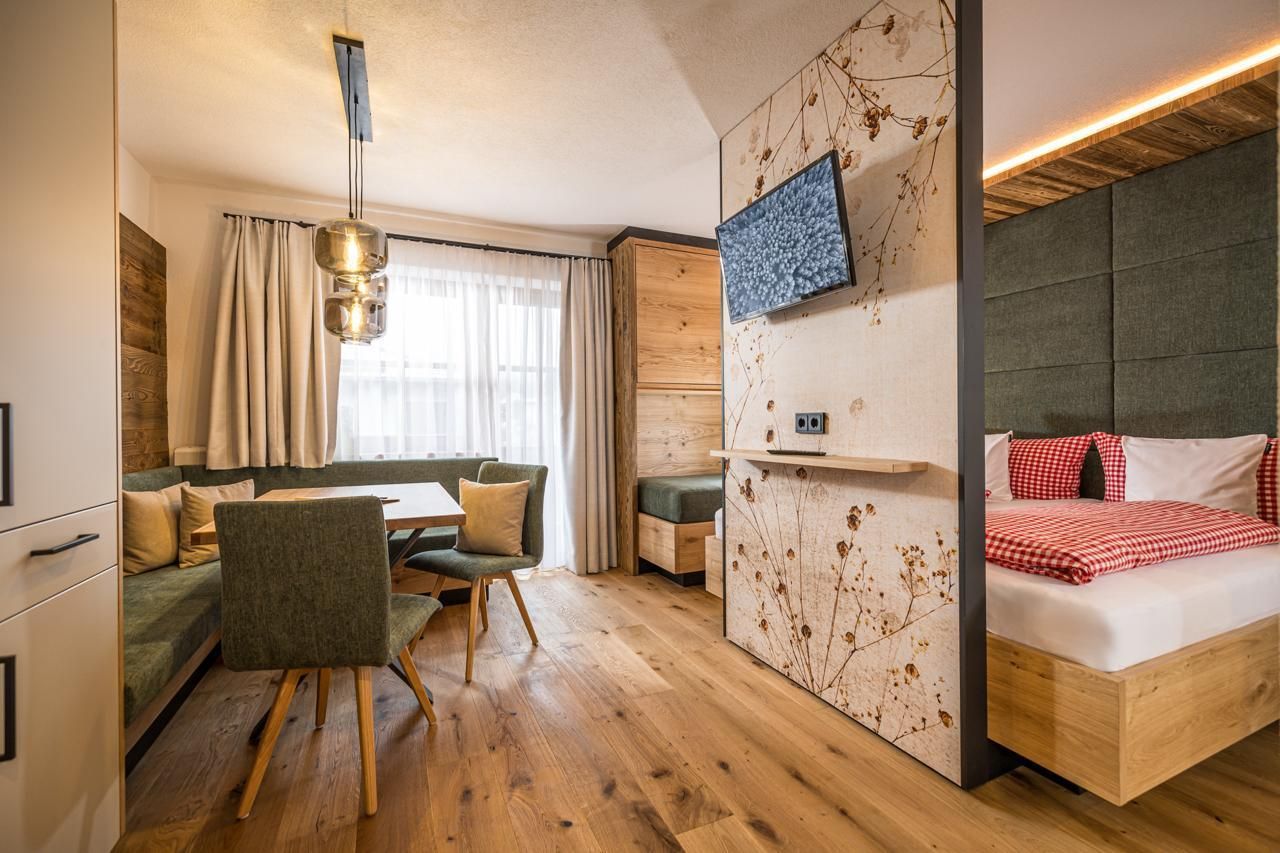 A modern room with a cozy dining area and a comfortable bed. Large windows provide plenty of daylight and a pleasant atmosphere.