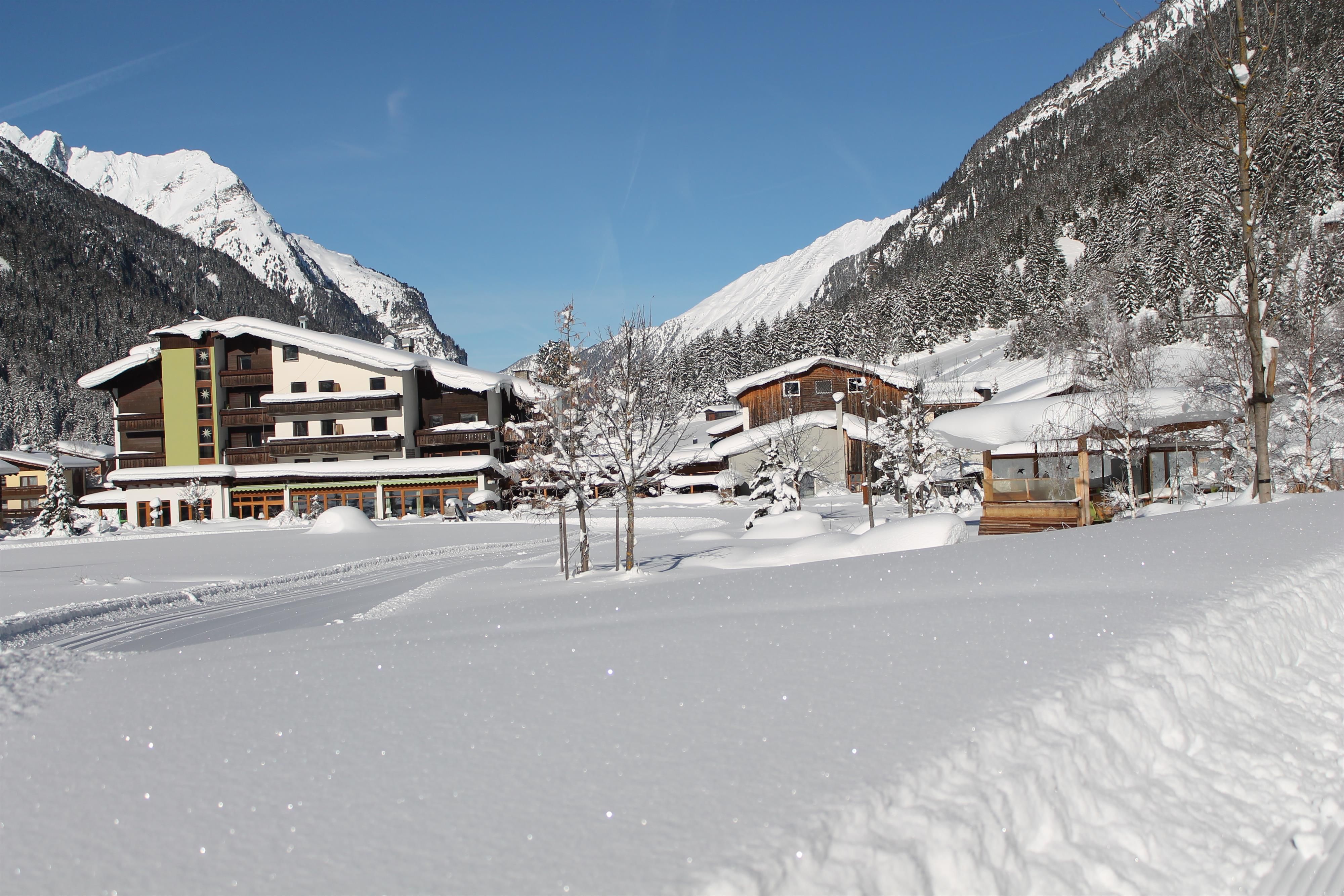 A snowy landscape with a hotel and mountains in the background. The sky is clear and blue.