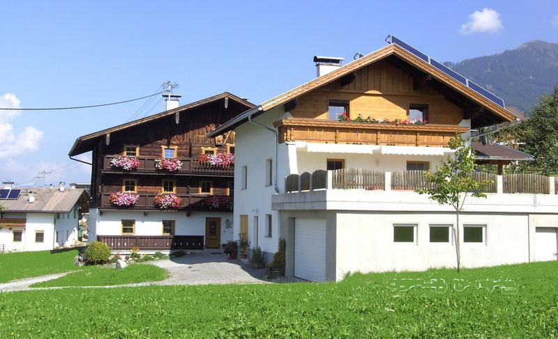 A charming house in Alpine style with wooden cladding and blooming balconies. The green meadow and mountain backdrop give the surroundings an idyllic atmosphere.