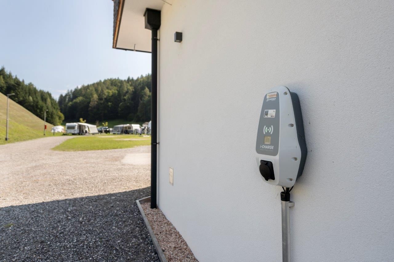 A charging station for electric vehicles on an outer wall. In the background, trees and a path are visible.