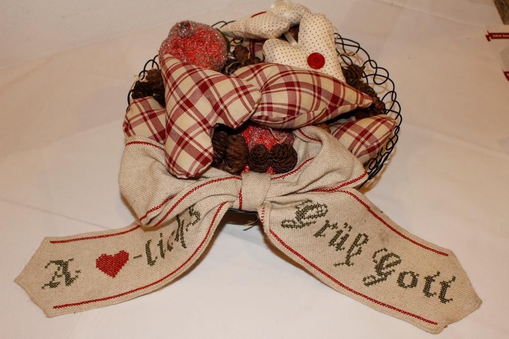 A woven basket with a decorative ribbon and various colorful ornaments. The ribbon bears the inscription "A l(i)ds Grüß Gott."