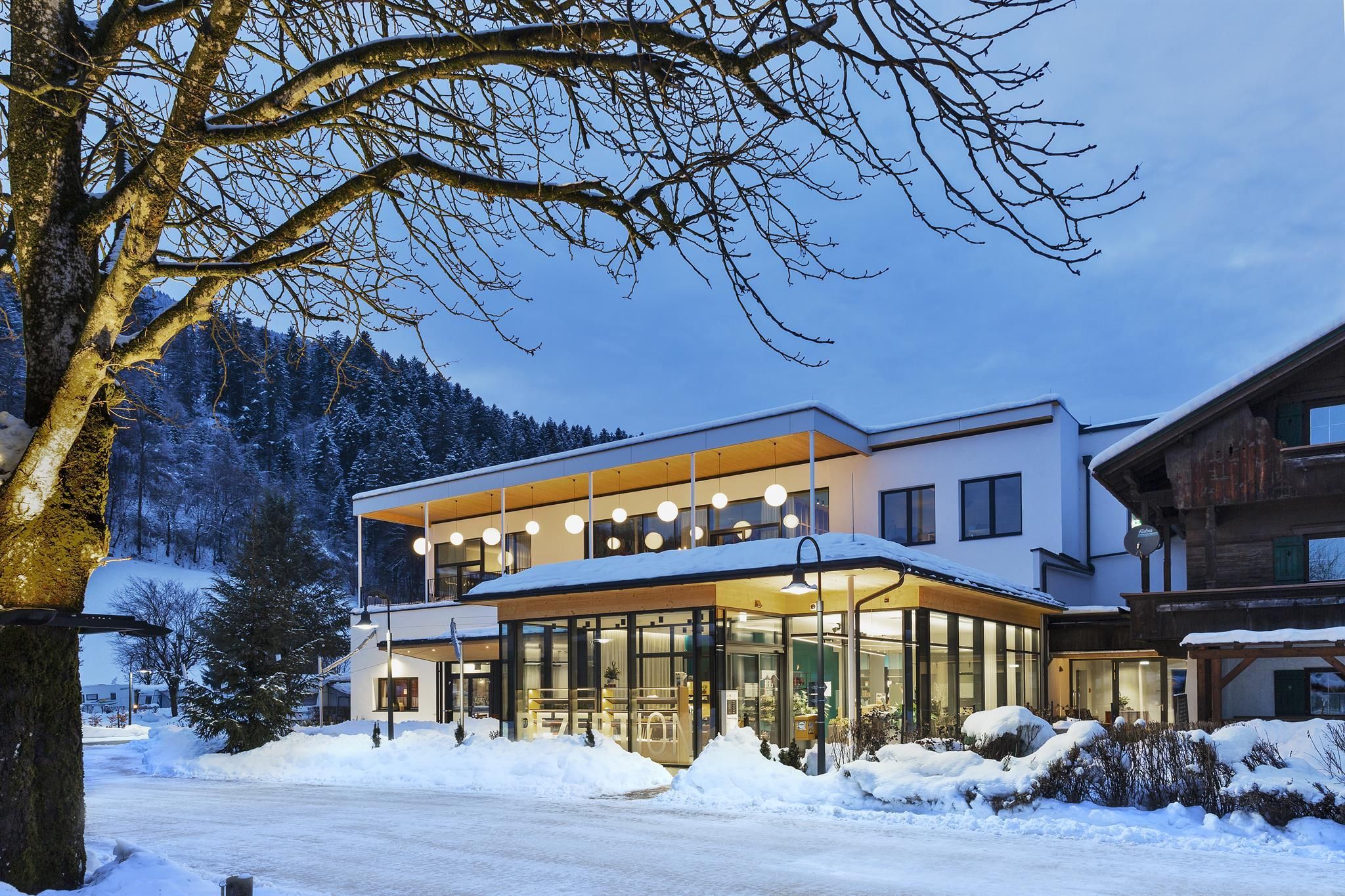A modern building in a snow-covered landscape. In the background, snowy mountains and trees can be seen.