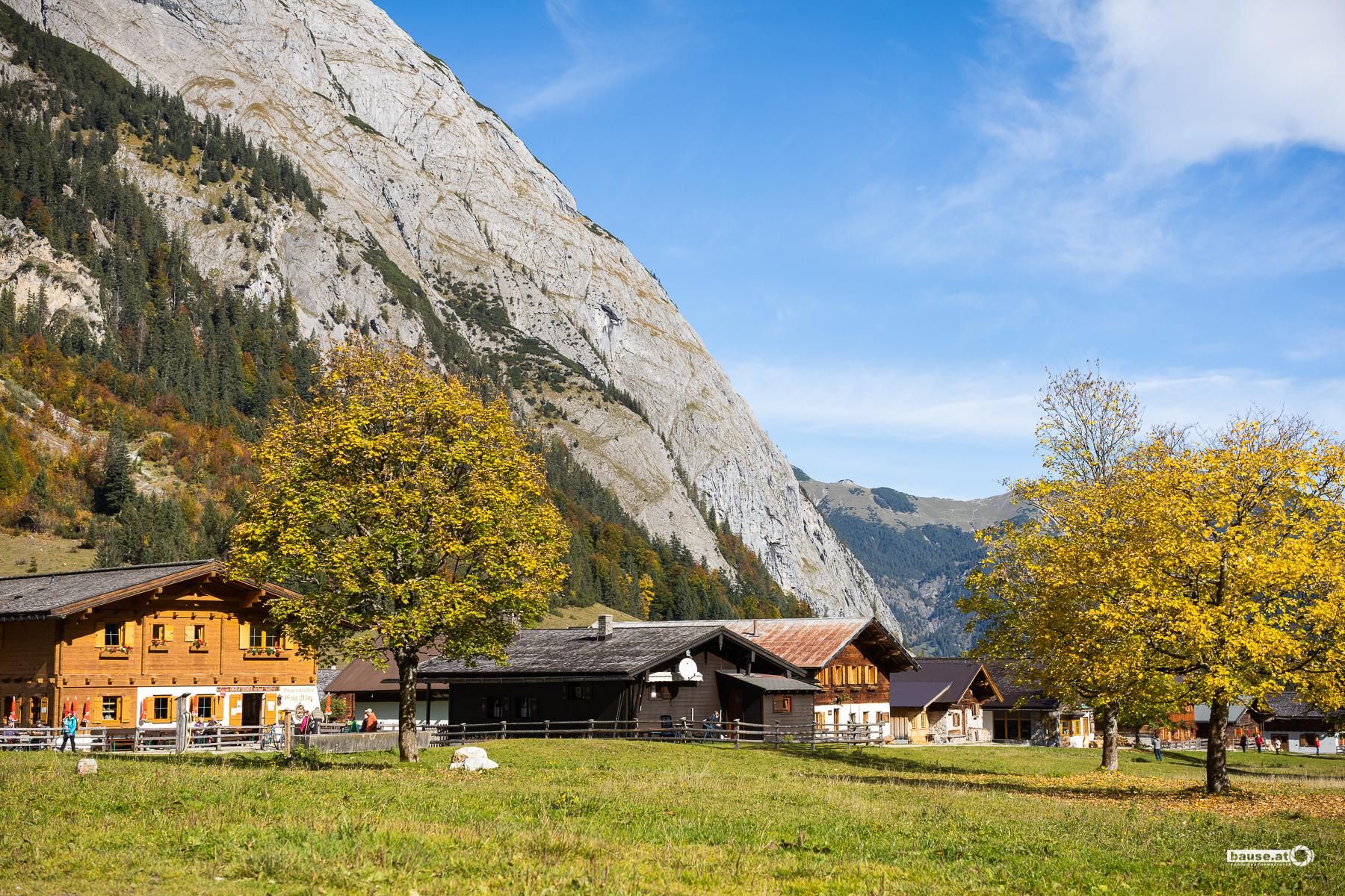 A tranquil alpine landscape with traditional chalets and beautiful trees. In the background, an imposing mountain rises under a clear blue sky.