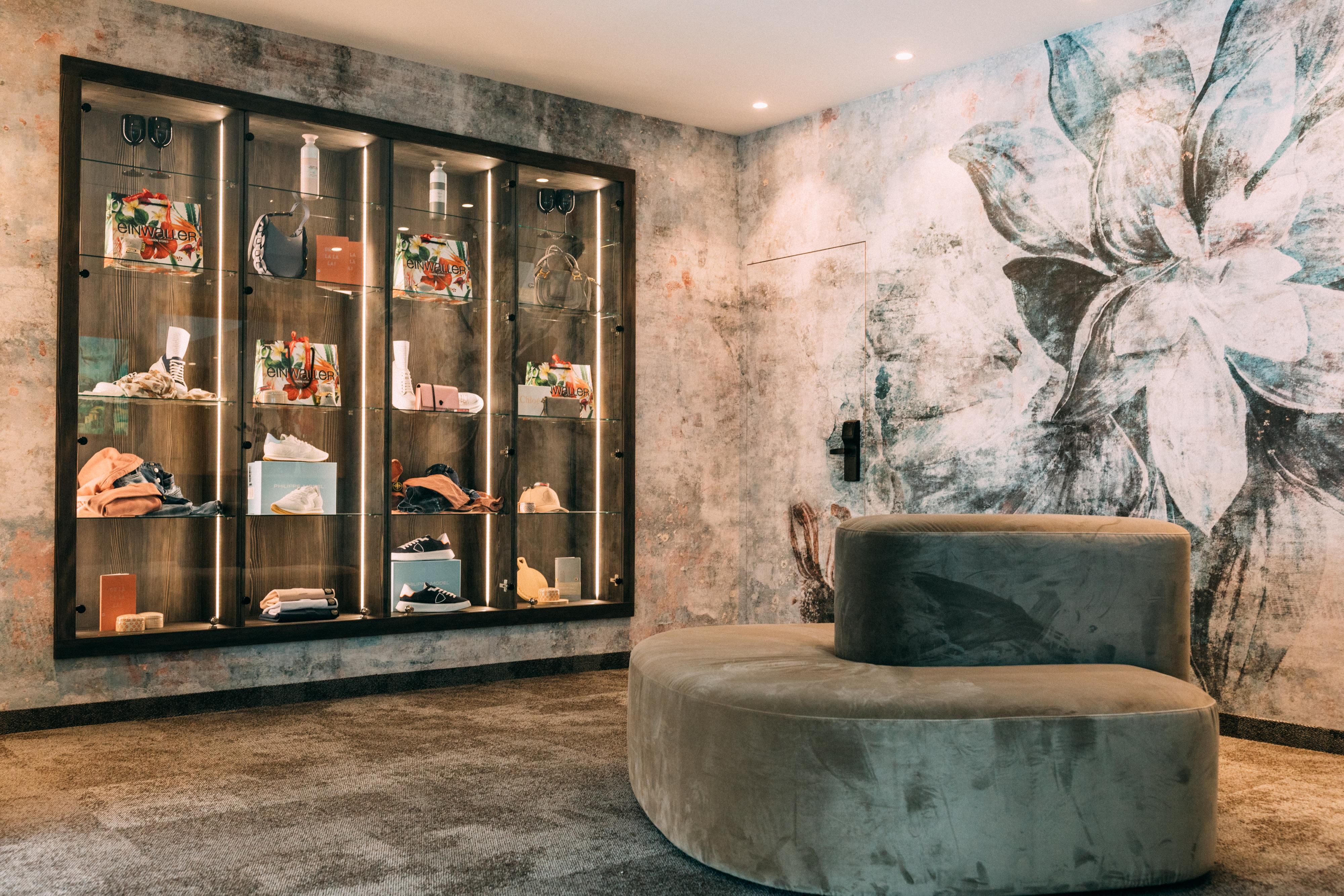 A stylish interior with a round seating area and a glass showcase. The wall is decorated with a floral motif, while the showcase displays various accessories.