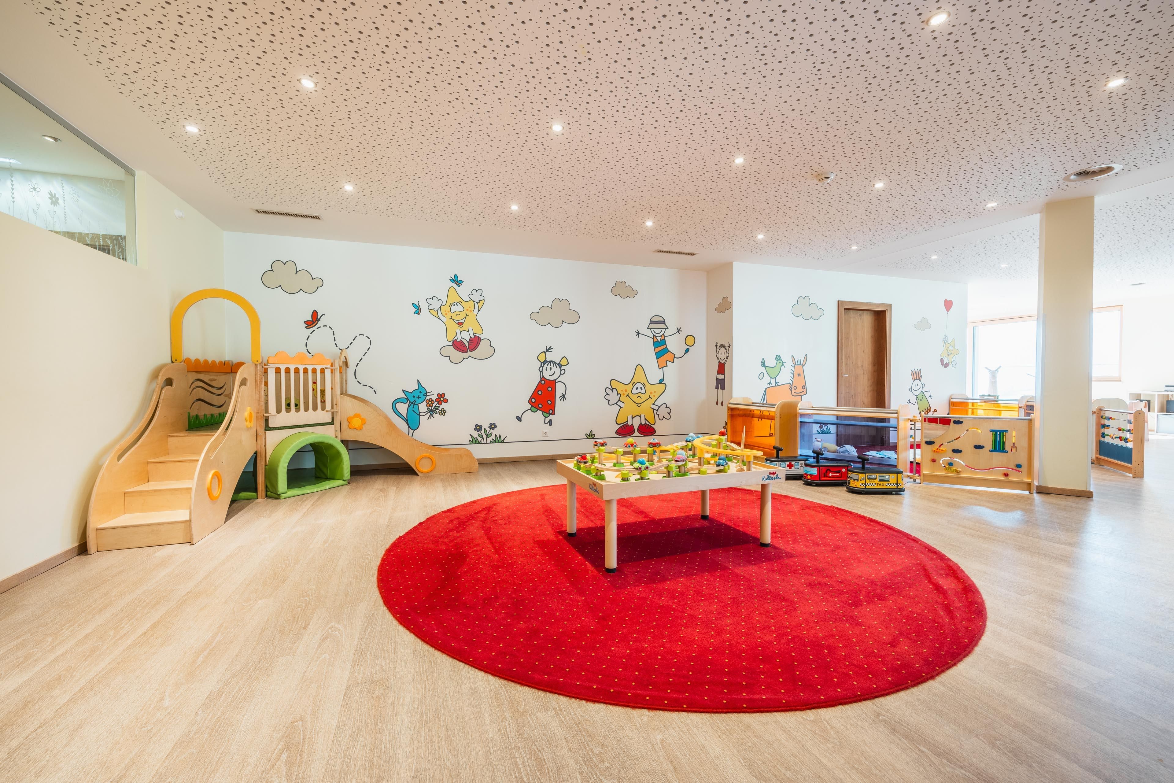 A colorful children's club with a red carpet, slide, and ball track. Colorful wall motifs create an inviting atmosphere.