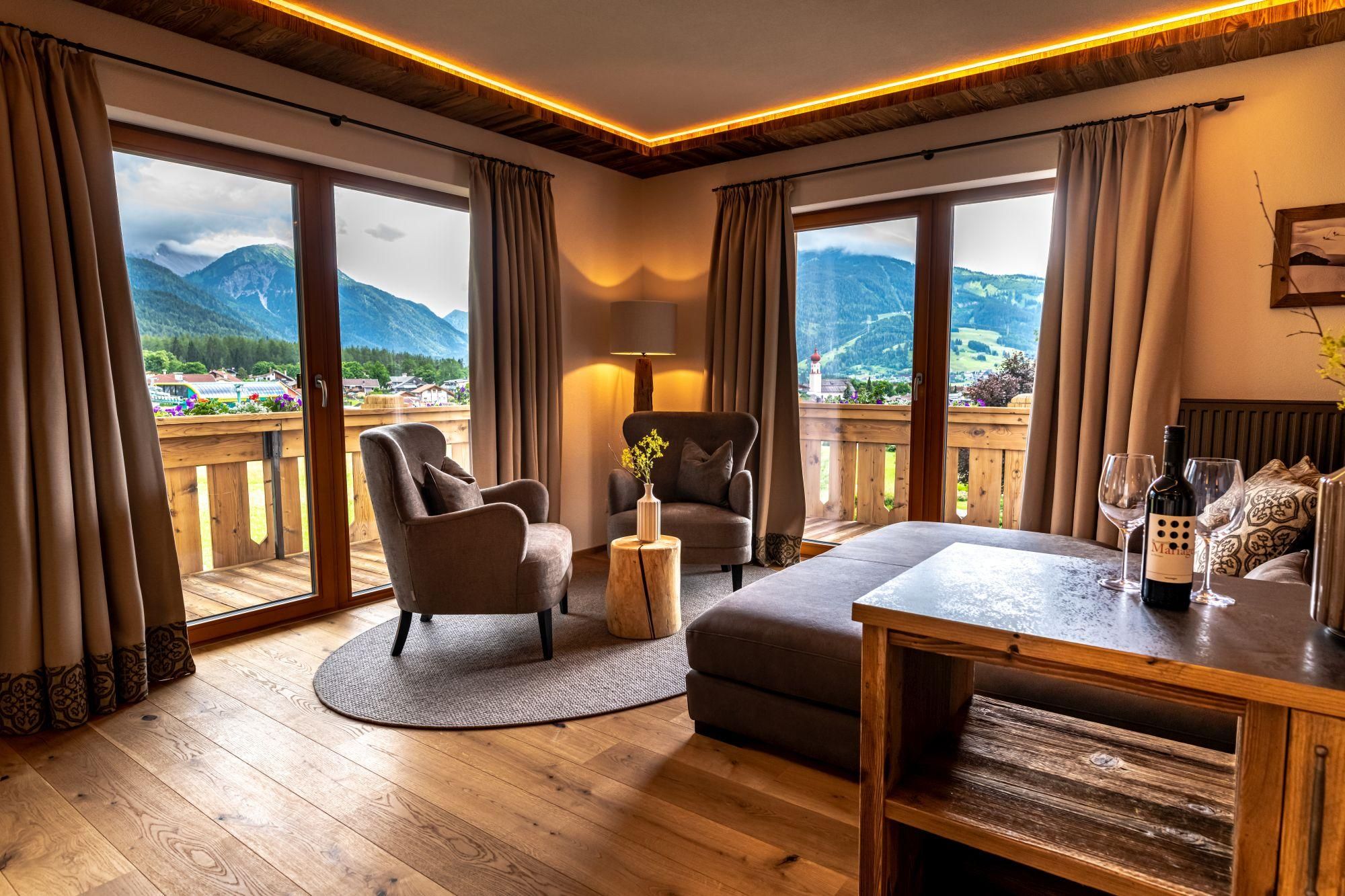 A cozy living area with two armchairs and a table. The view through the windows shows a picturesque mountain landscape.