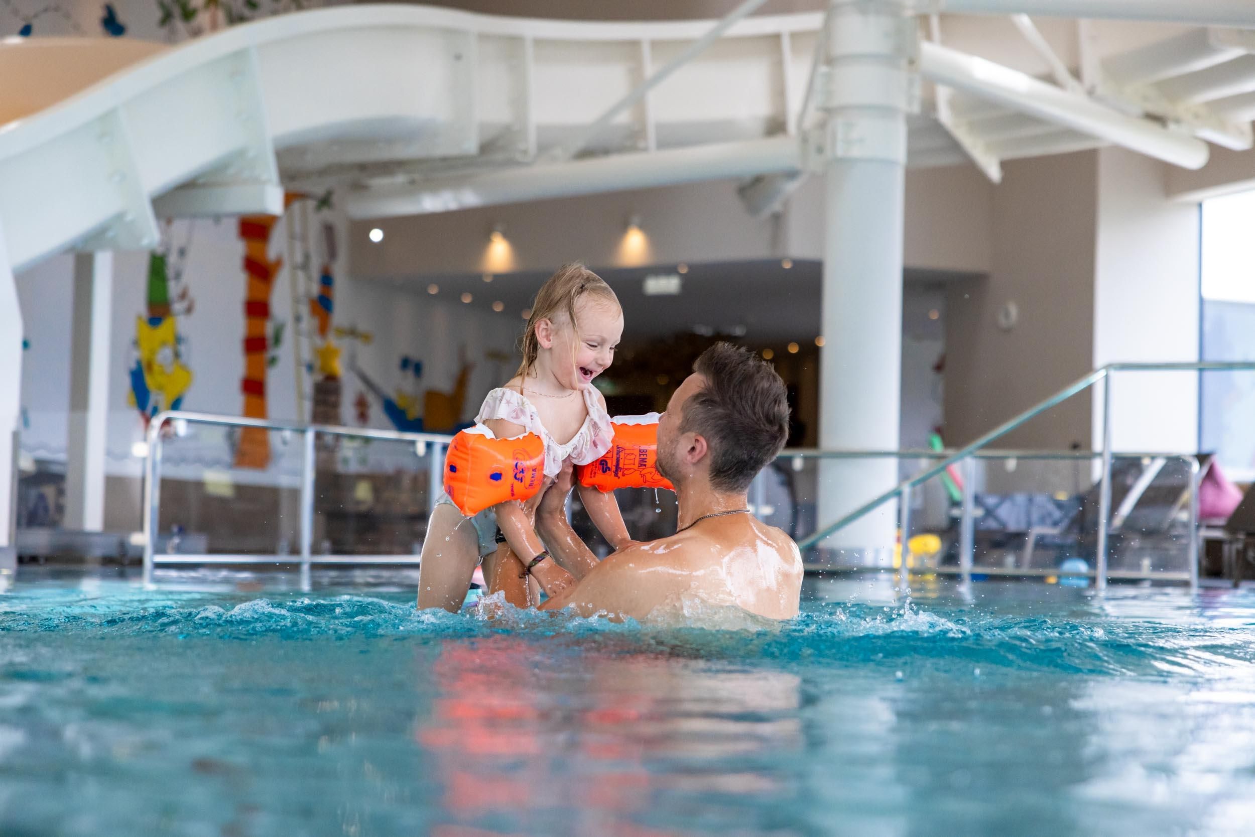 An adult joyfully plays with a child in the water in the family water world. Both are having fun and enjoying their time together.