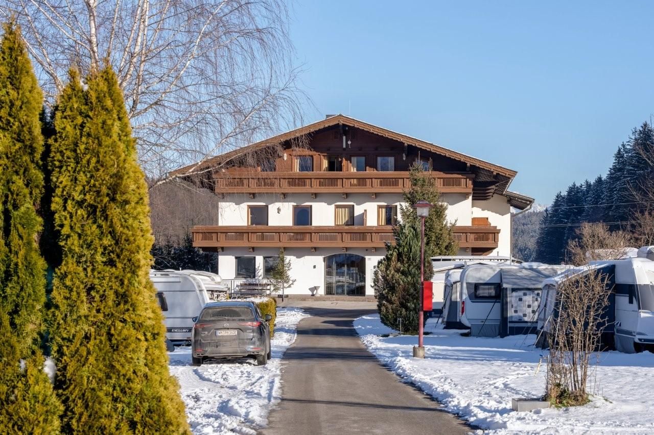 A charming building in alpine style, surrounded by snow and fir trees. The path leads to the entrance of the house, which stands in a quiet landscape.