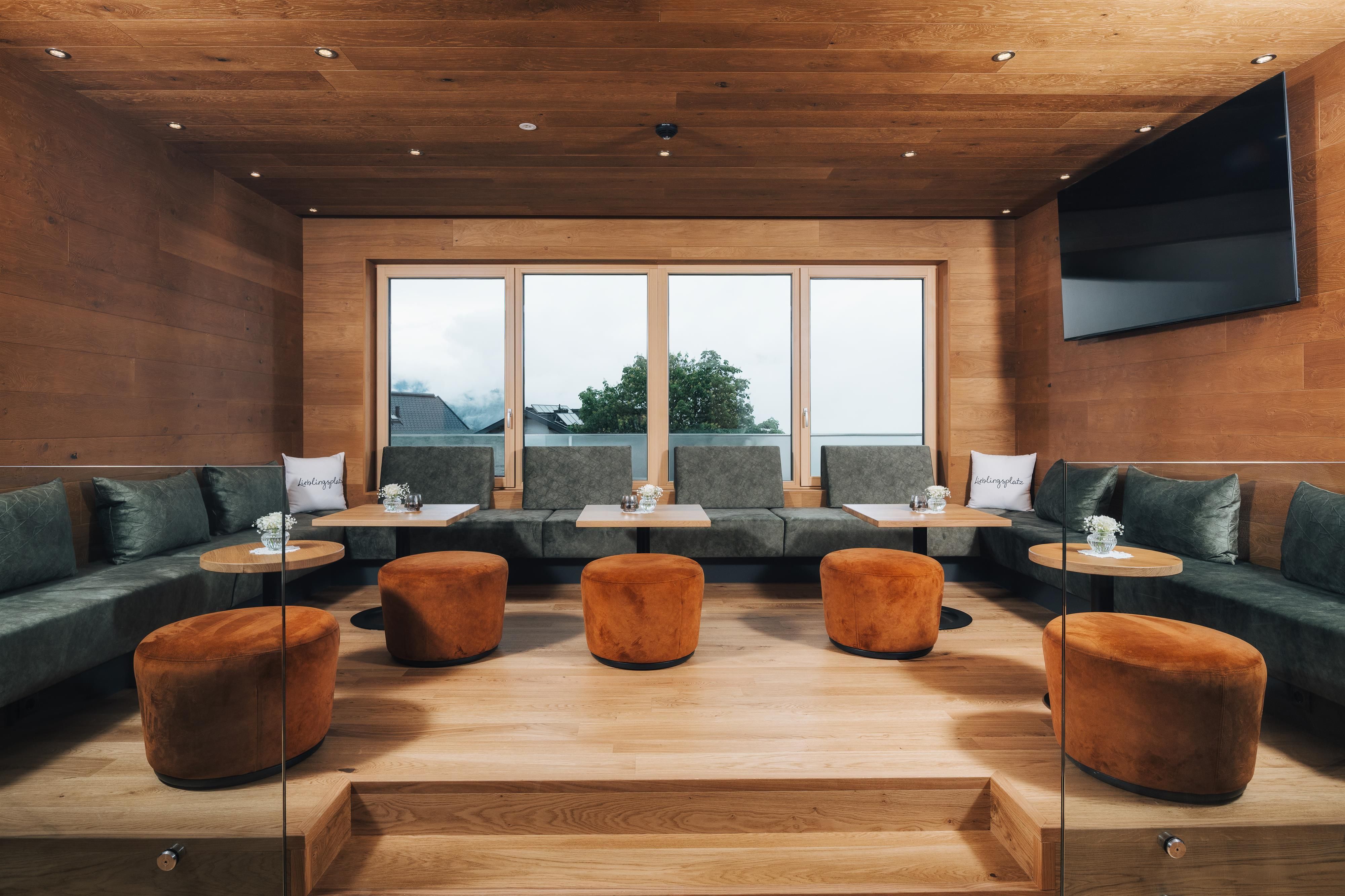 An inviting lounge area with green benches and orange stools. Large windows offer a view of the outdoors and provide plenty of daylight.