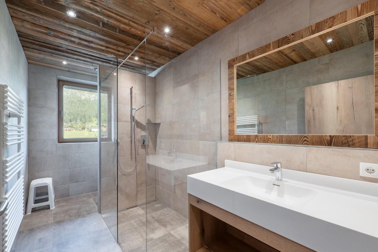 A modern bathroom with a walk-in glass shower and a large mirror. Bright tiles create a simple, elegant atmosphere.