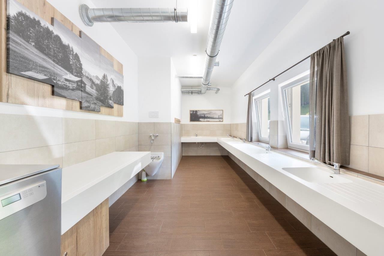 A modern bathroom with spacious sinks and bright tiles. Large windows provide plenty of daylight and a pleasant atmosphere.