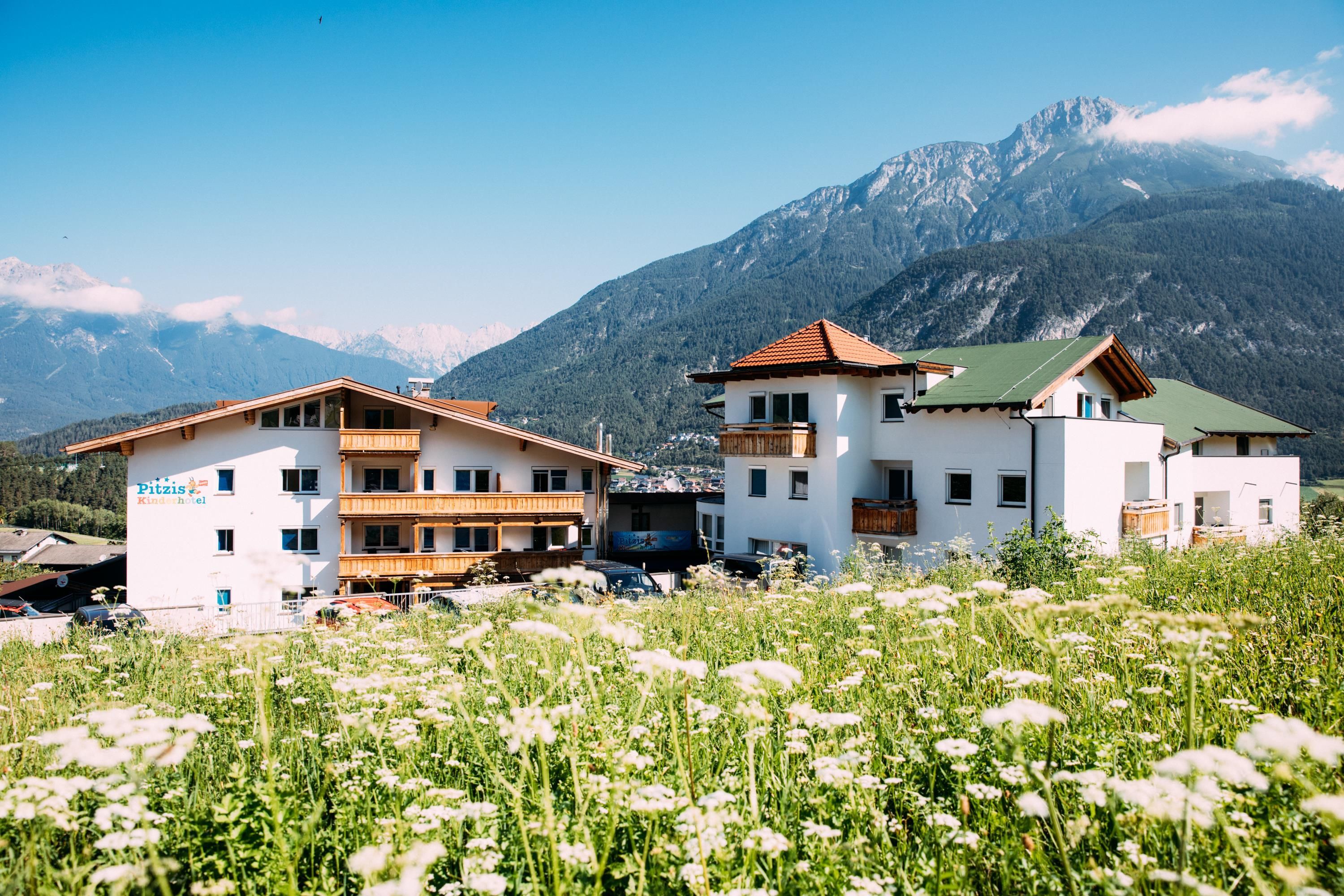 Unique alpine huts in a picturesque landscape. In the background, majestic mountains rise under a clear blue sky.