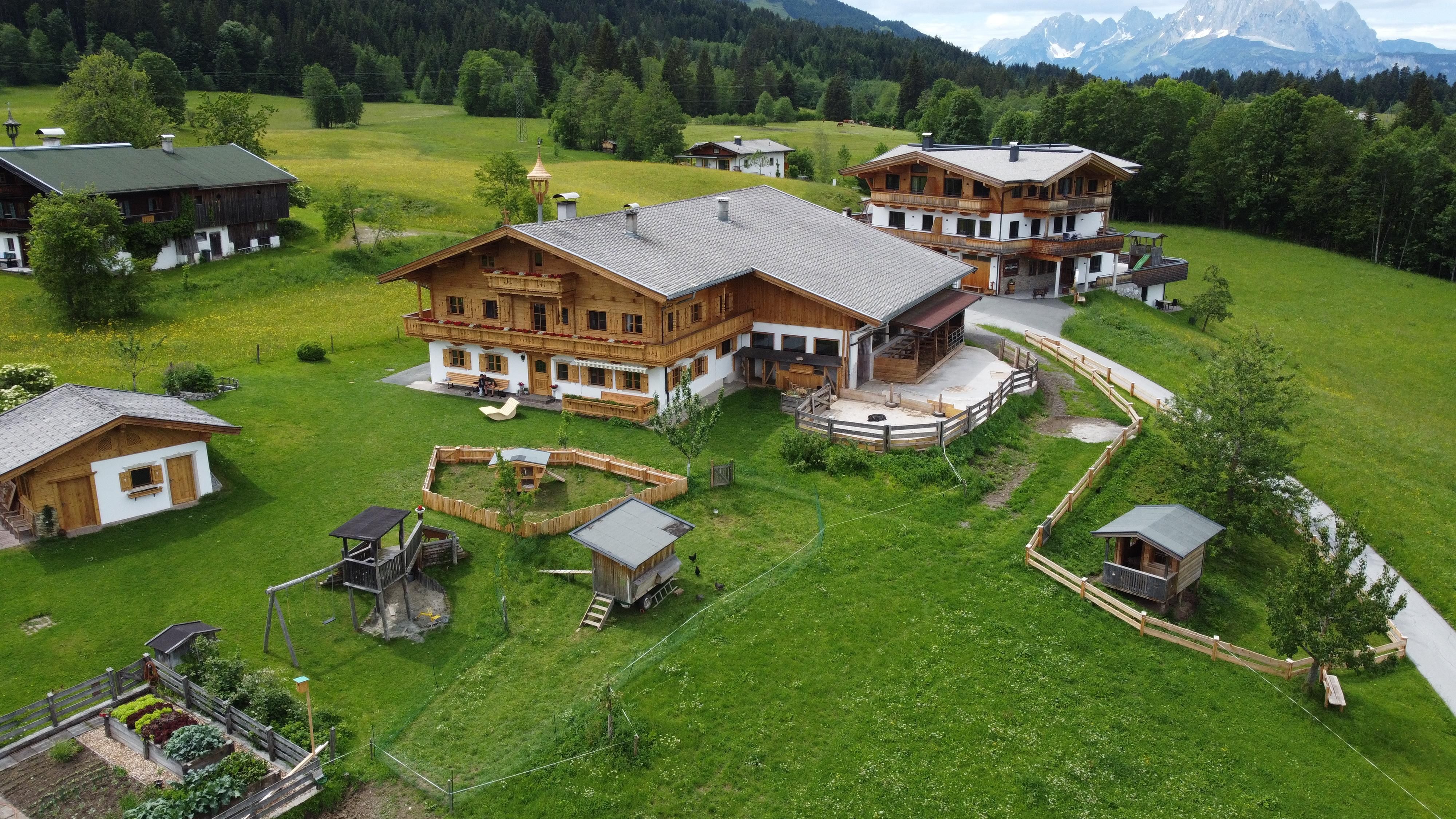 A beautiful estate with wooden houses in a green landscape. In the background, there are mountains and a clear sky.