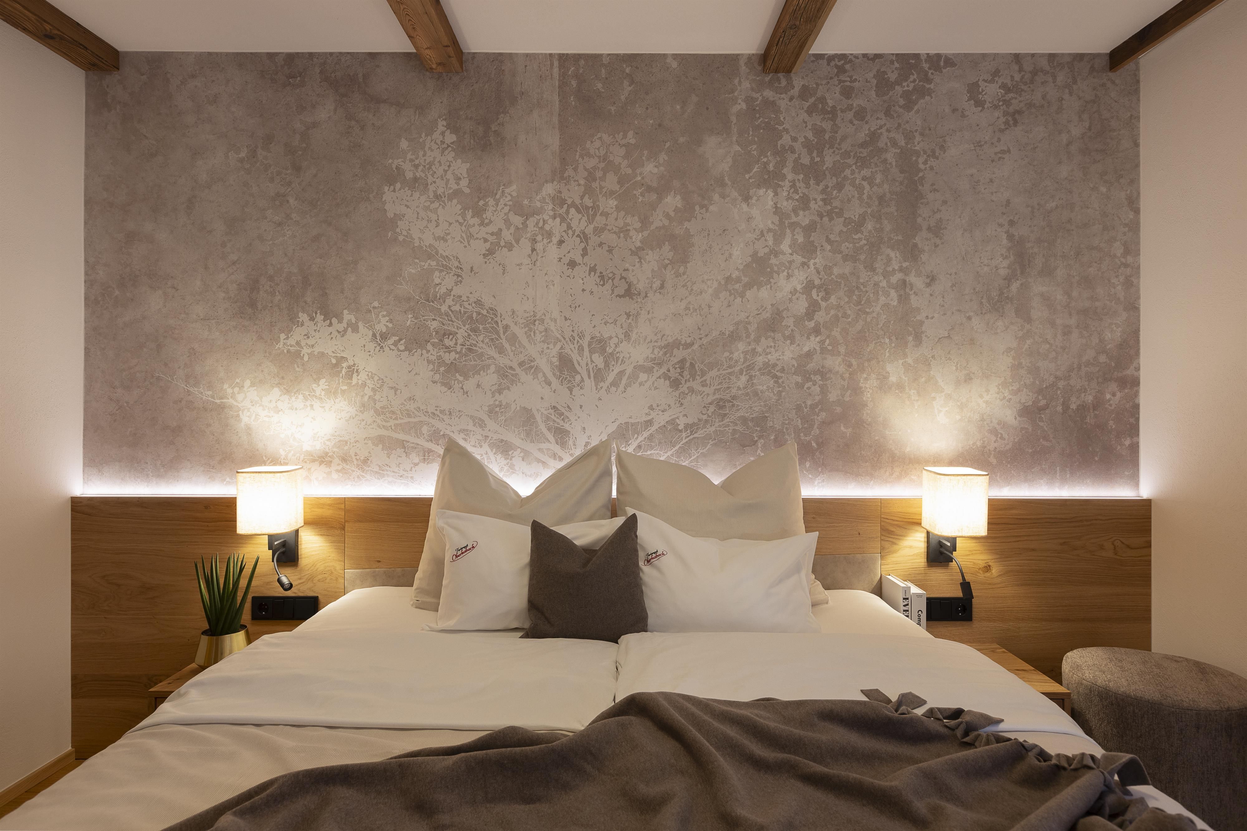 A stylish bedroom with a large bed and elegant lighting. The walls are adorned with a modern gray pattern.