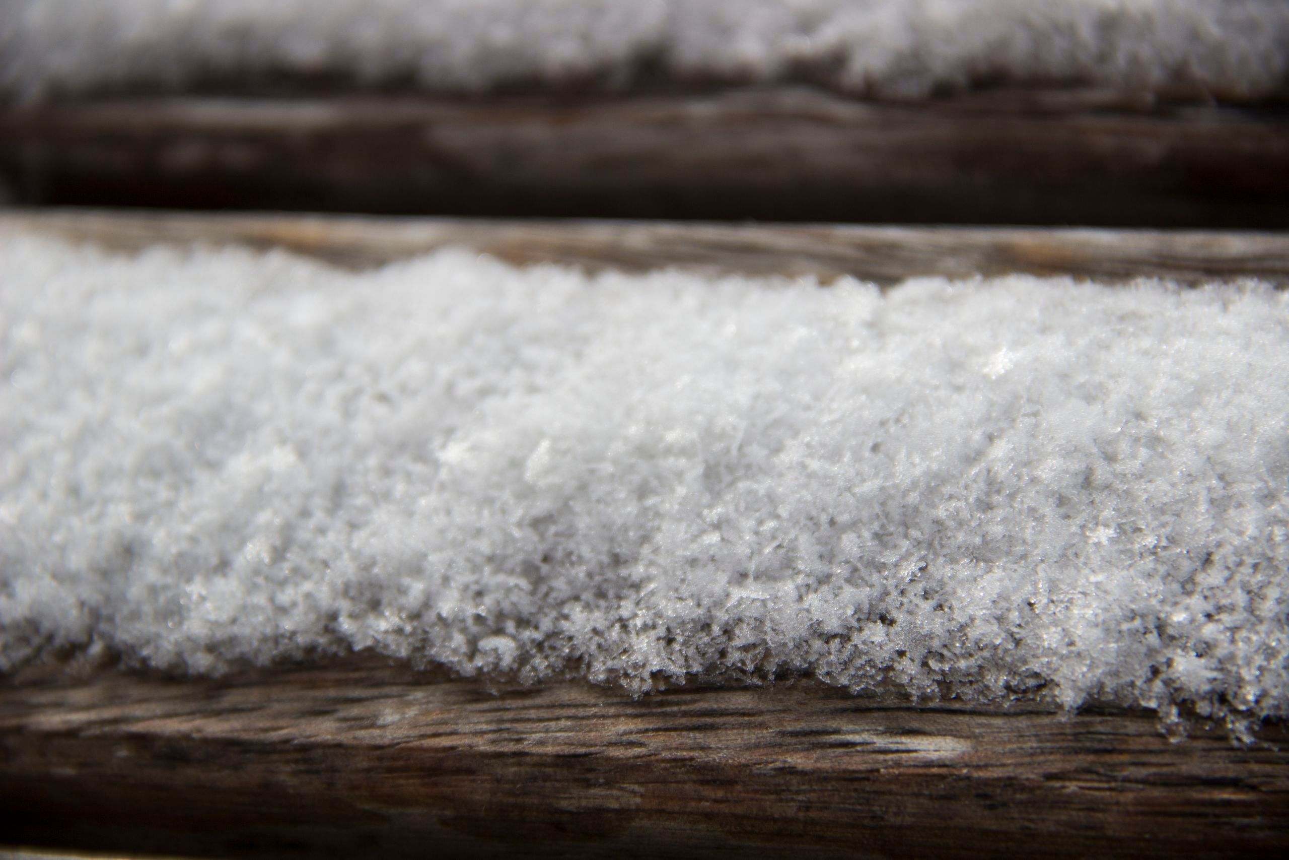 Nahaufnahme von Schnee auf einer Holzbank. Man erkennt die einzelnen Schneeflocken mit bloßen Auge.