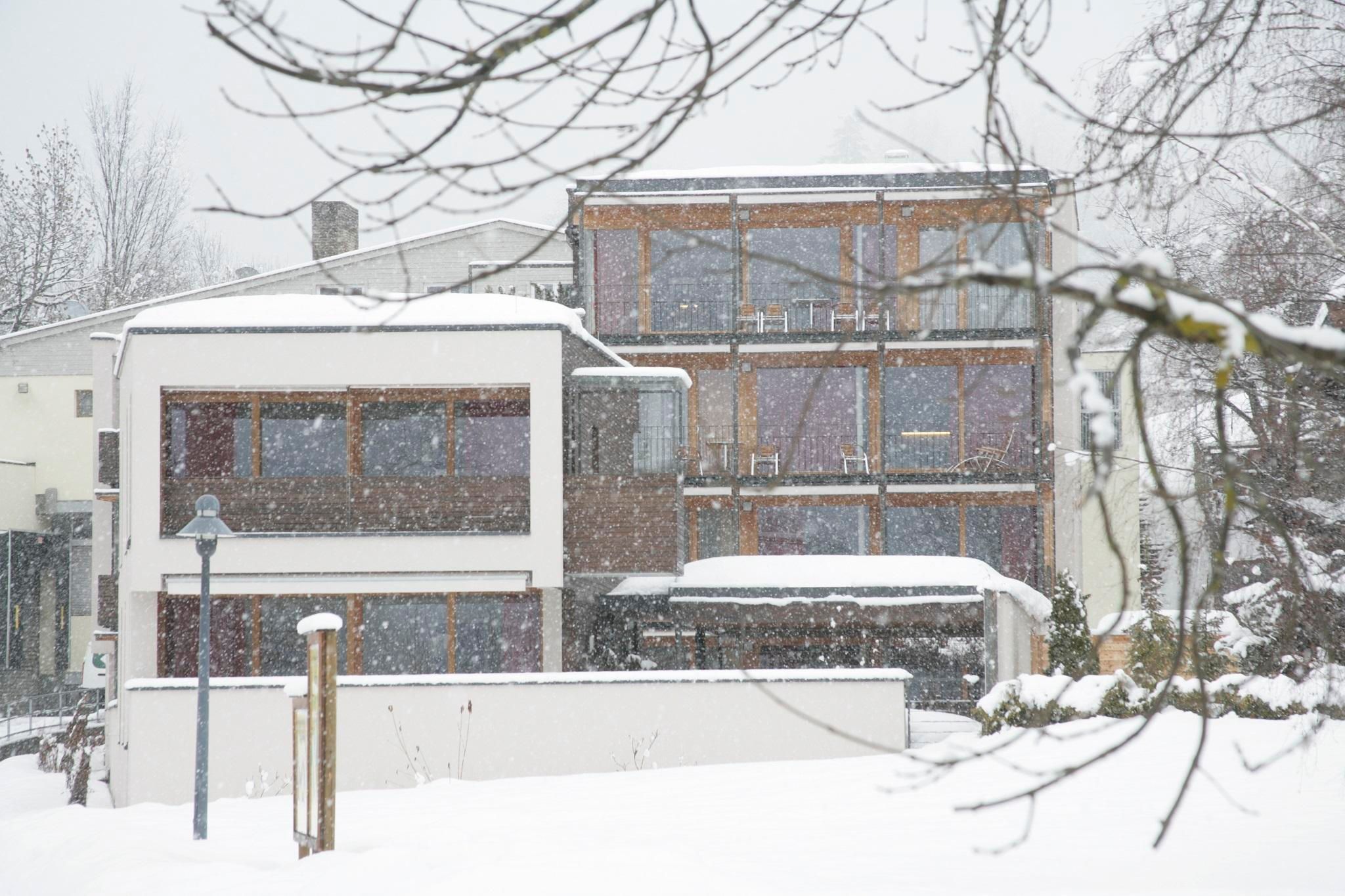 A modern building in the snow, surrounded by a wintry landscape. Visible snowfall creates a calm, wintery atmosphere.