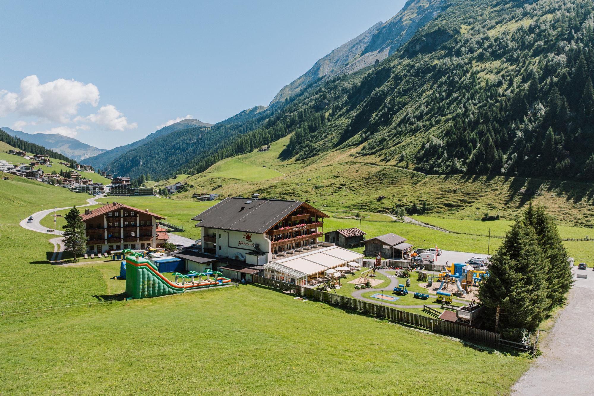 A picturesque mountain landscape with green meadows and beautiful cottages. In the foreground, there is a recreational area with playgrounds and slides.