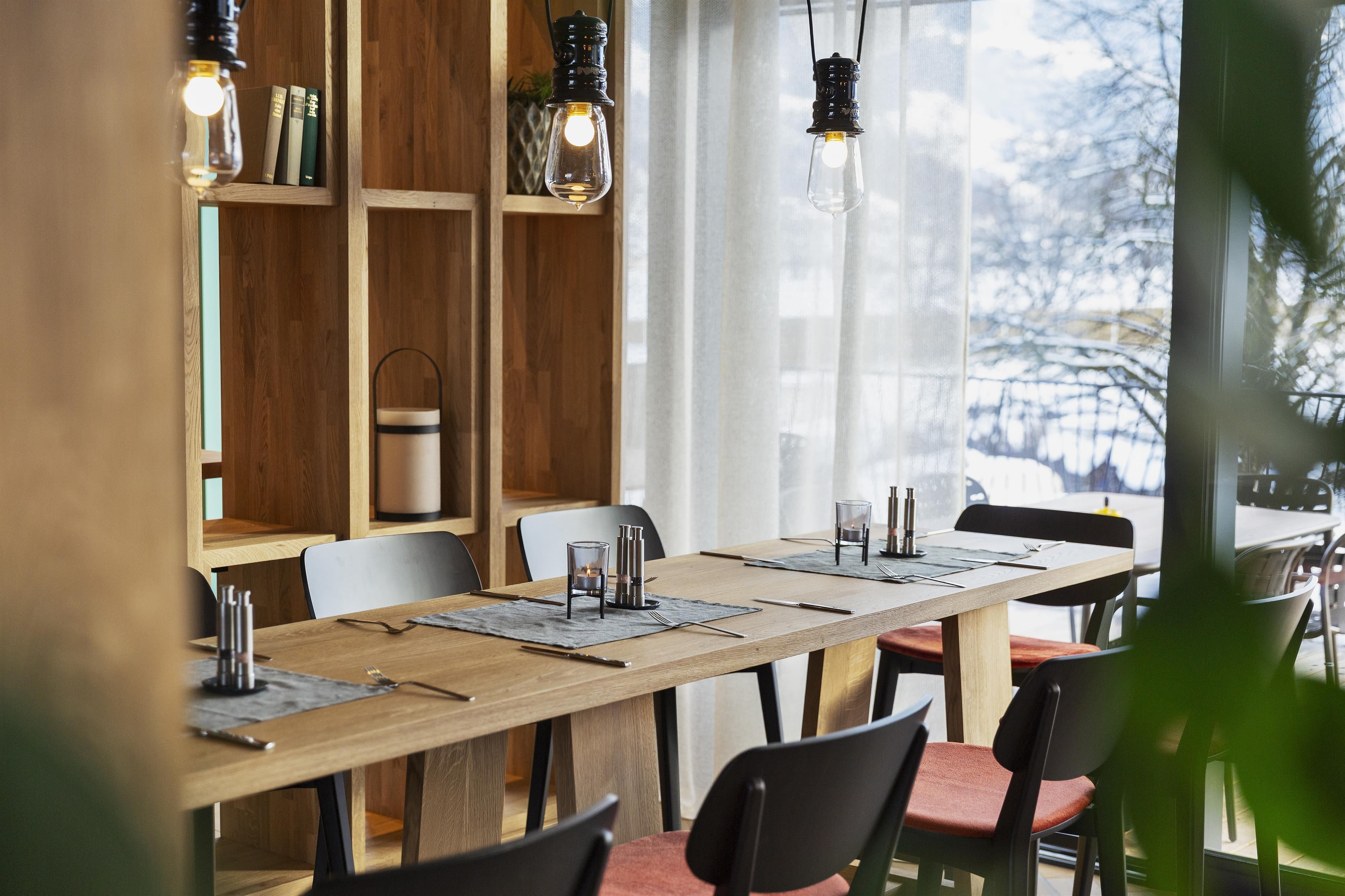 A modern restaurant with wooden tables and stylish chairs. Large windows let in plenty of light and offer a view outside.