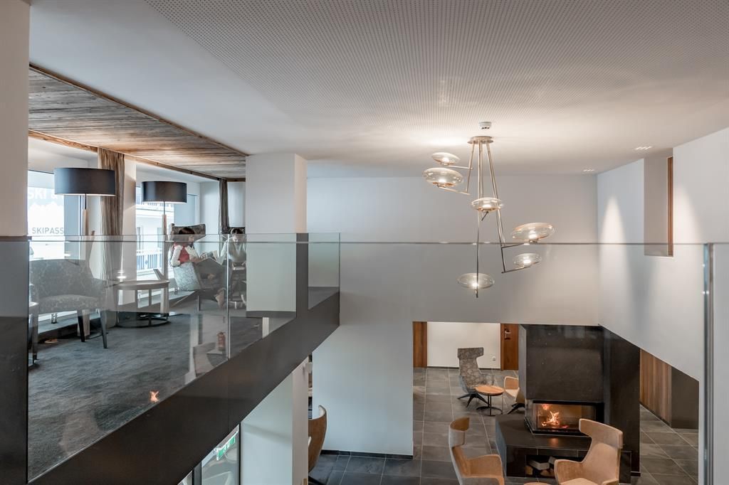 A modern room with stylish furniture and an open fireplace. Large windows let in plenty of daylight.