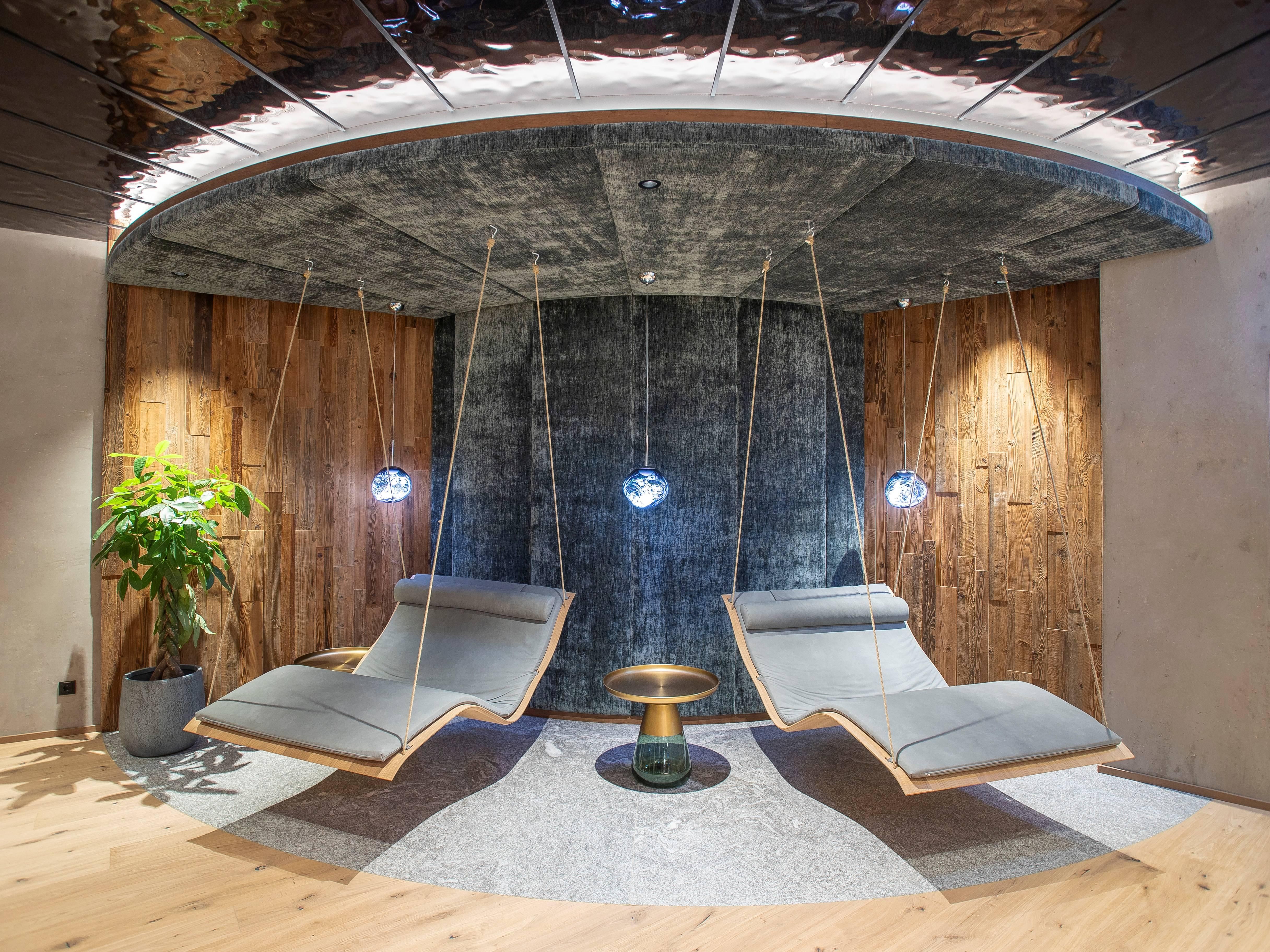 A modern interior with two hanging loungers and a cozy atmosphere. A plant and stylish lighting complement the design.