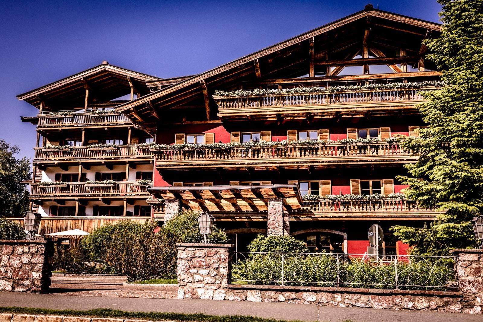 A beautiful wooden house in Alpine style with several balconies. Surrounded by trees and green plants.