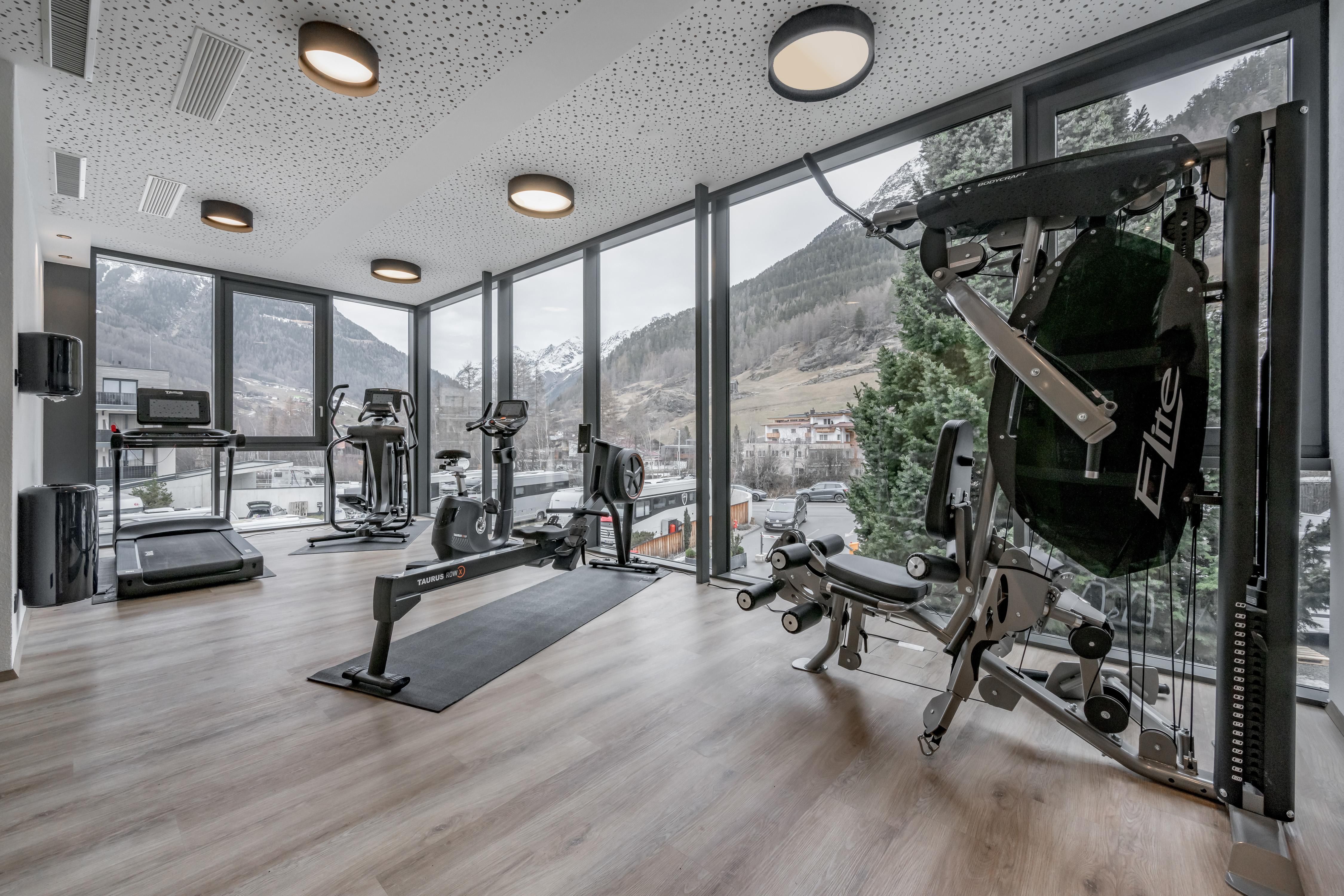A modern gym with large windows and a view of the mountains. The equipment includes various fitness machines and plenty of space for training.