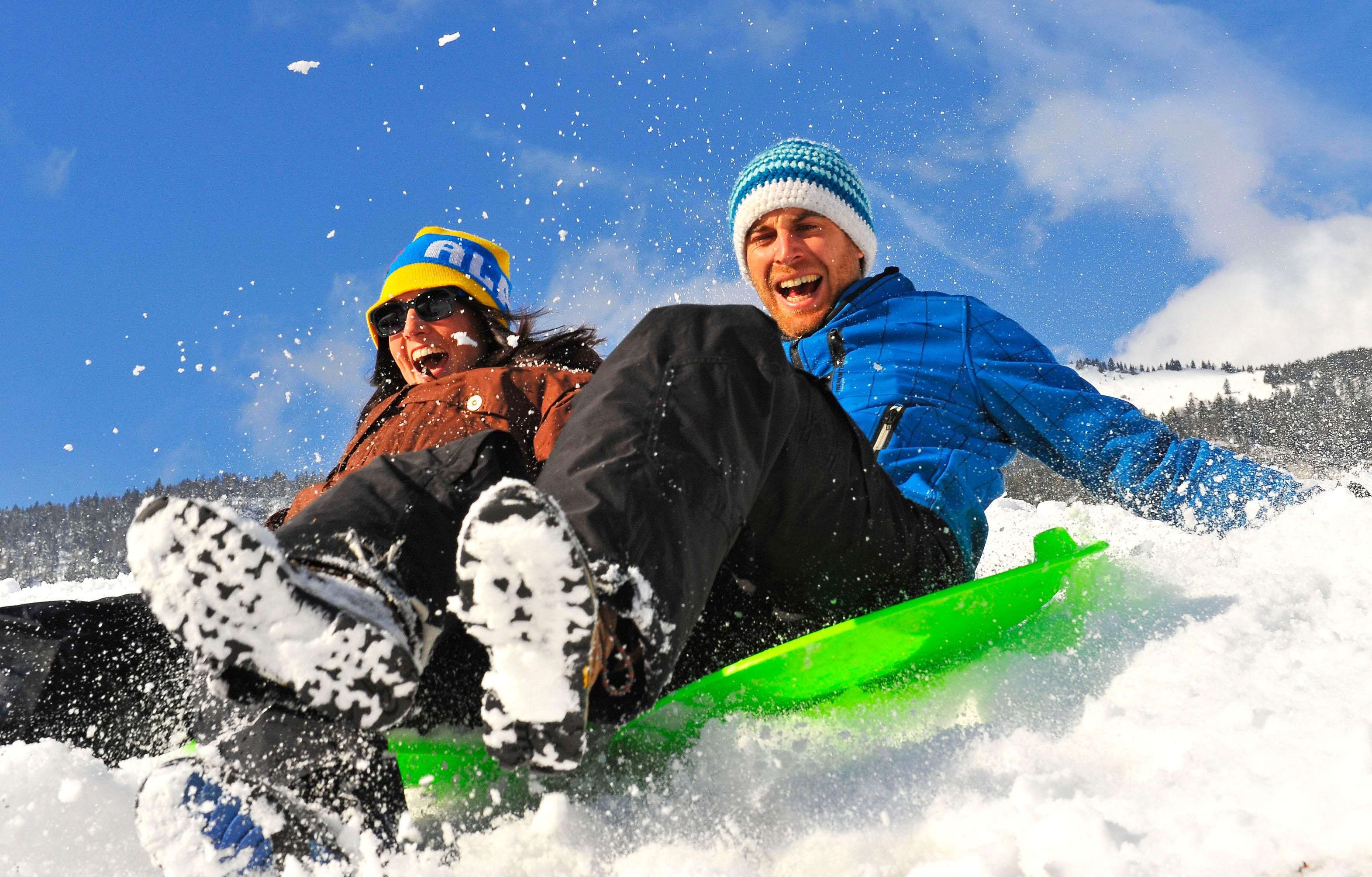 Two people are having fun sledding in the snow. They are wearing cheerful winter clothes and smiling.