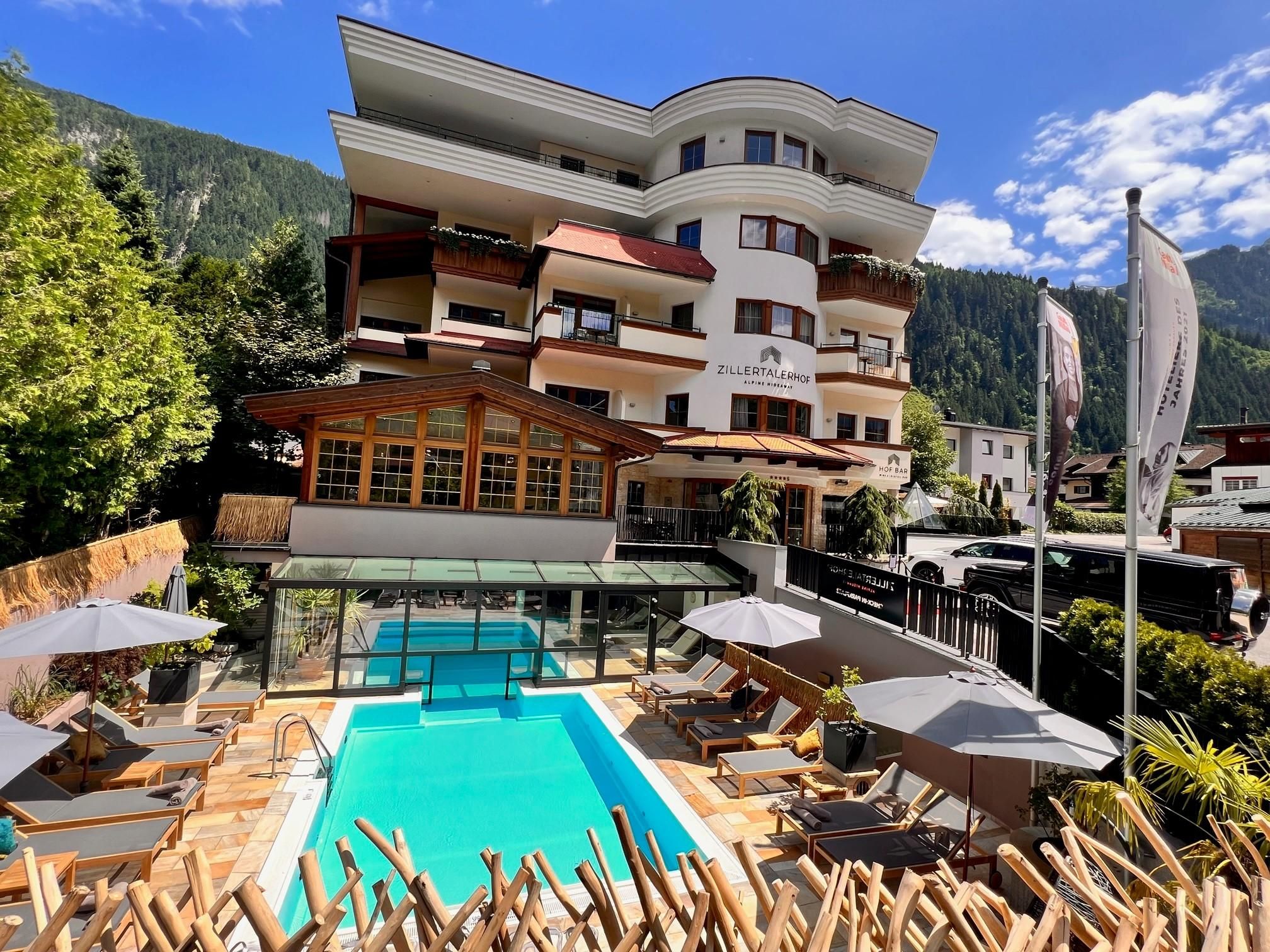 A modern design hotel with a casual pool area. In the background, mountains and a blue sky are visible.