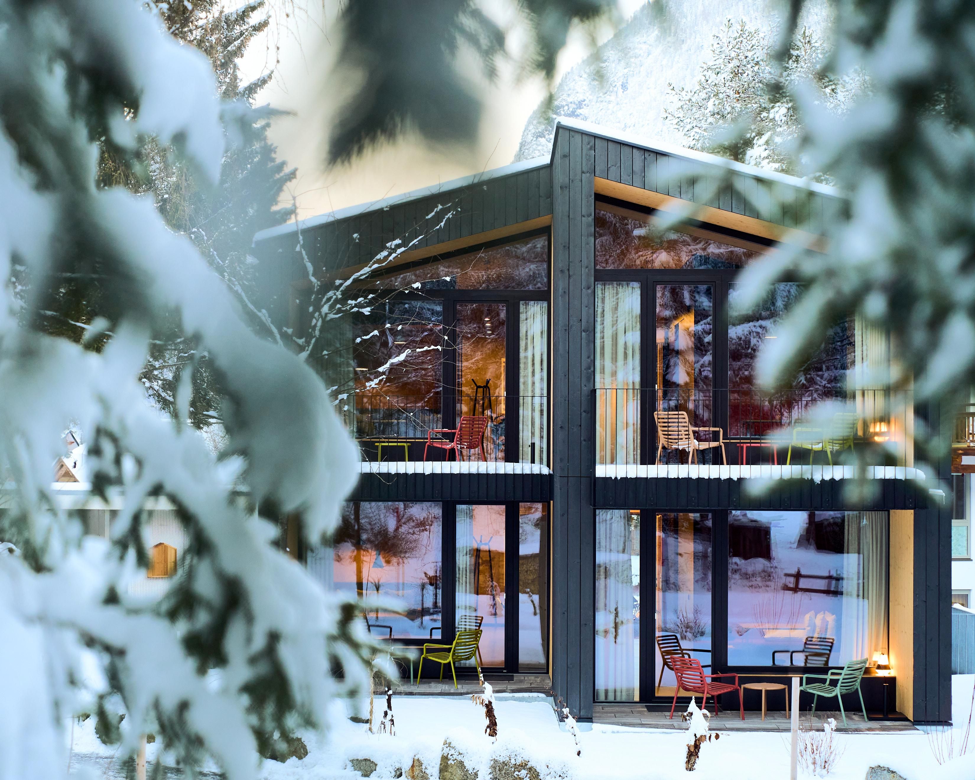 A modern, snow-covered house in a winter landscape. Large windows provide a glimpse of the cozy atmosphere inside.
