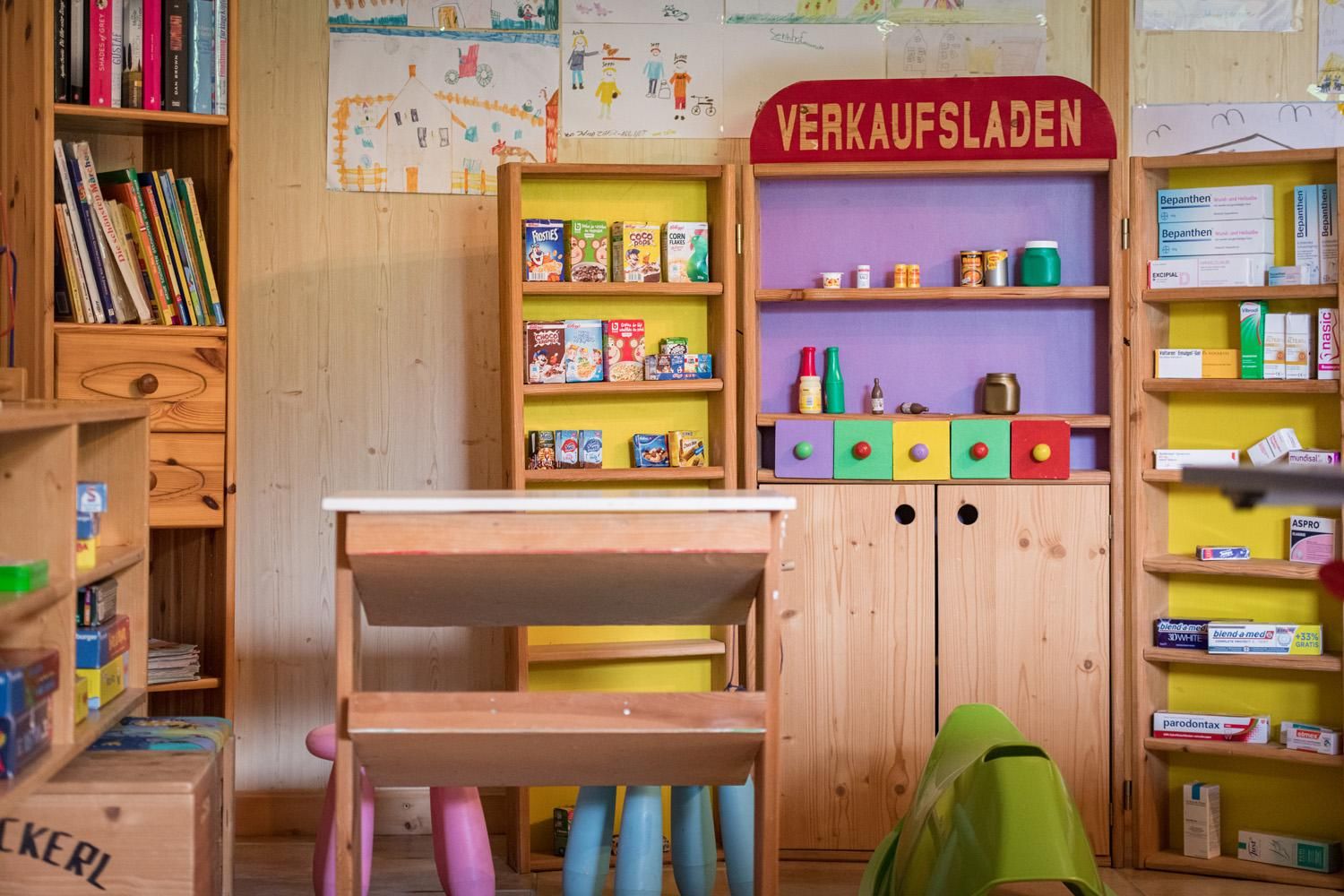 A child-friendly sales stand with colorful shelves full of toy packages. Next to the stand is a small table with chairs.